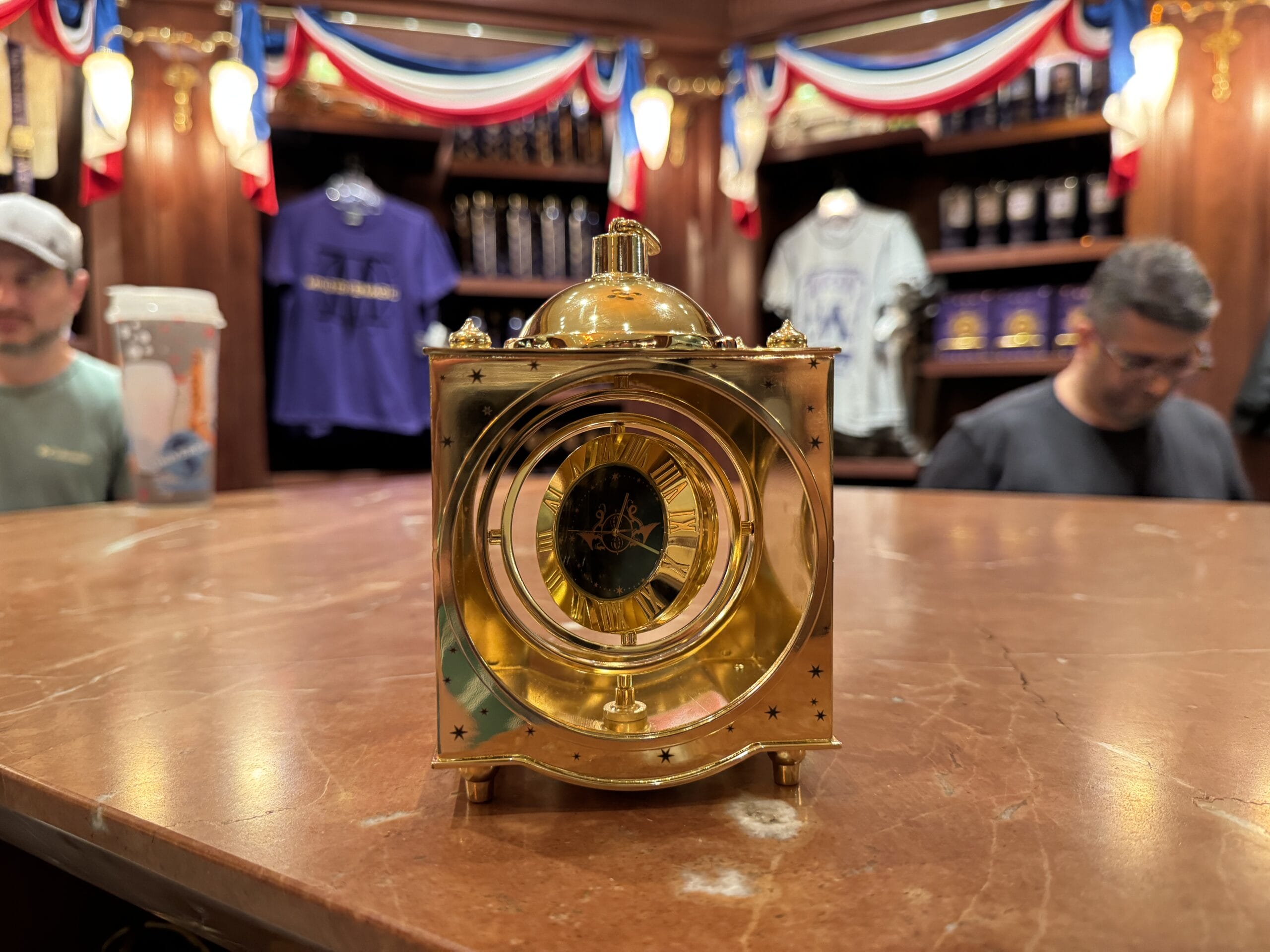 A gold clock with Roman numerals sits by Wizarding World of Harry Potter merchandise in a shop with red, white, and blue bunting.