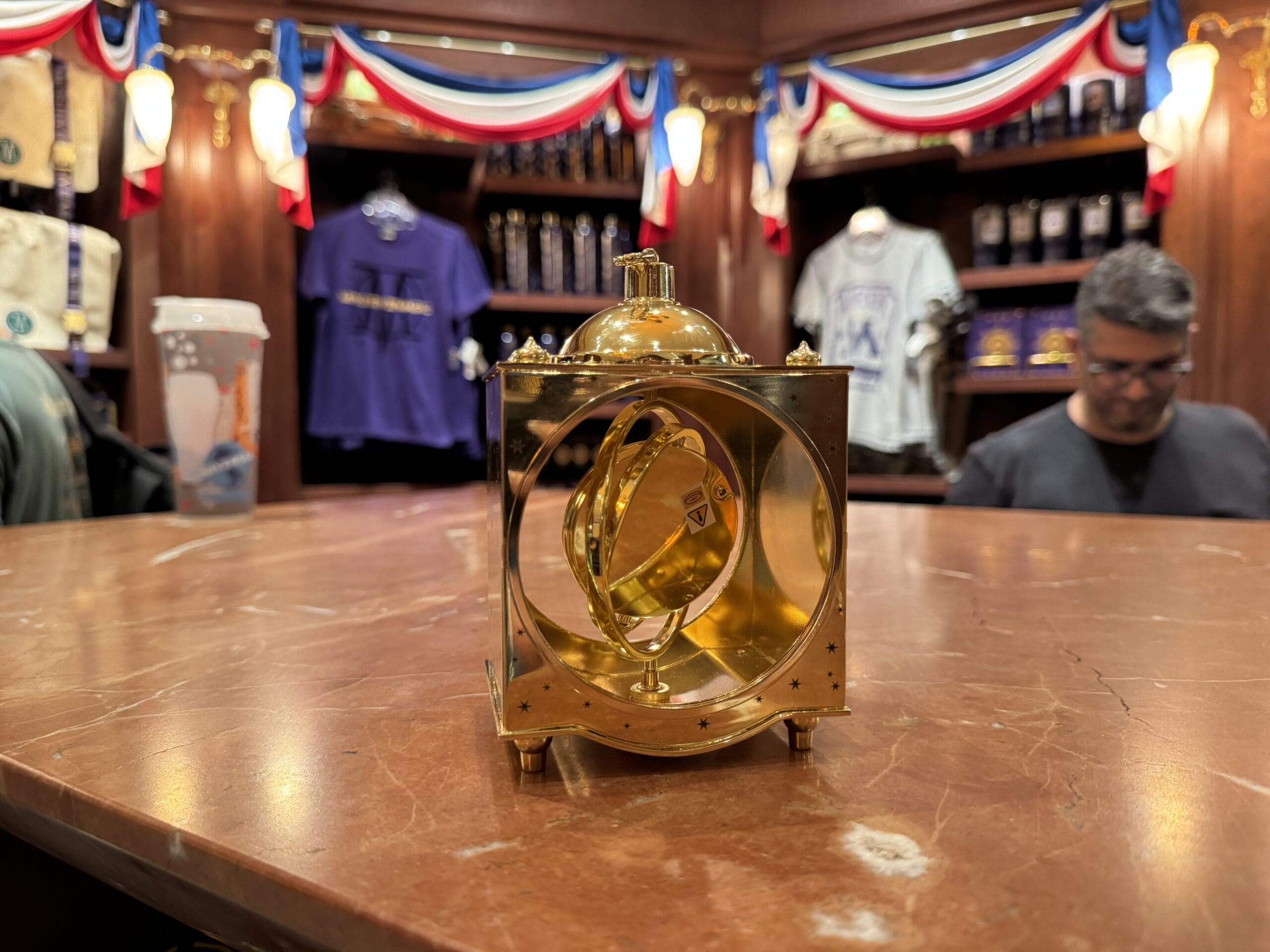 A golden time-turner display sits on a marble counter, surrounded by Wizarding World merchandise in the shop’s background.