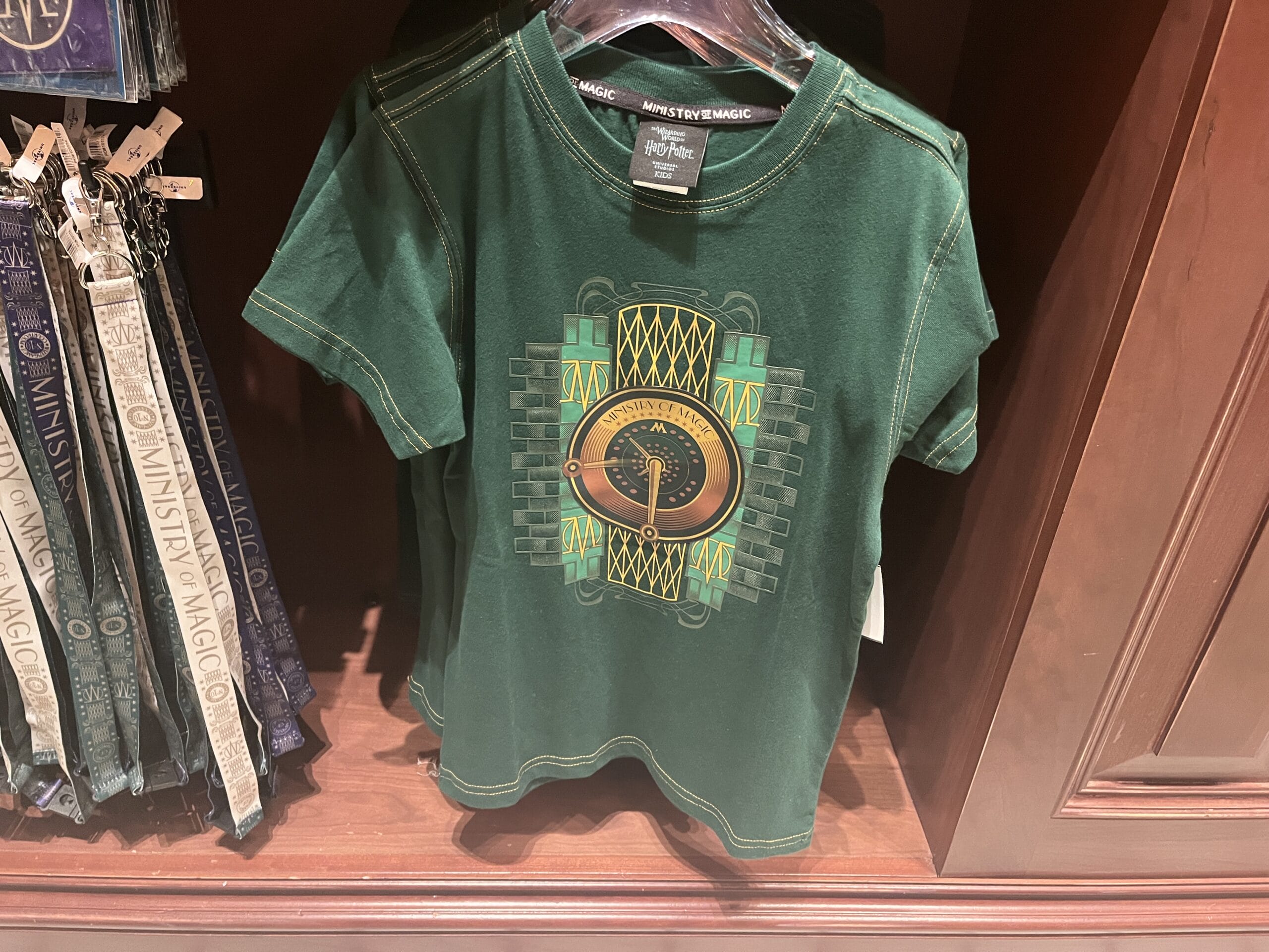 Green t-shirt with a stylized snake and Harry Potter "Ministry of Magic" logo displayed on a wooden shelf.
