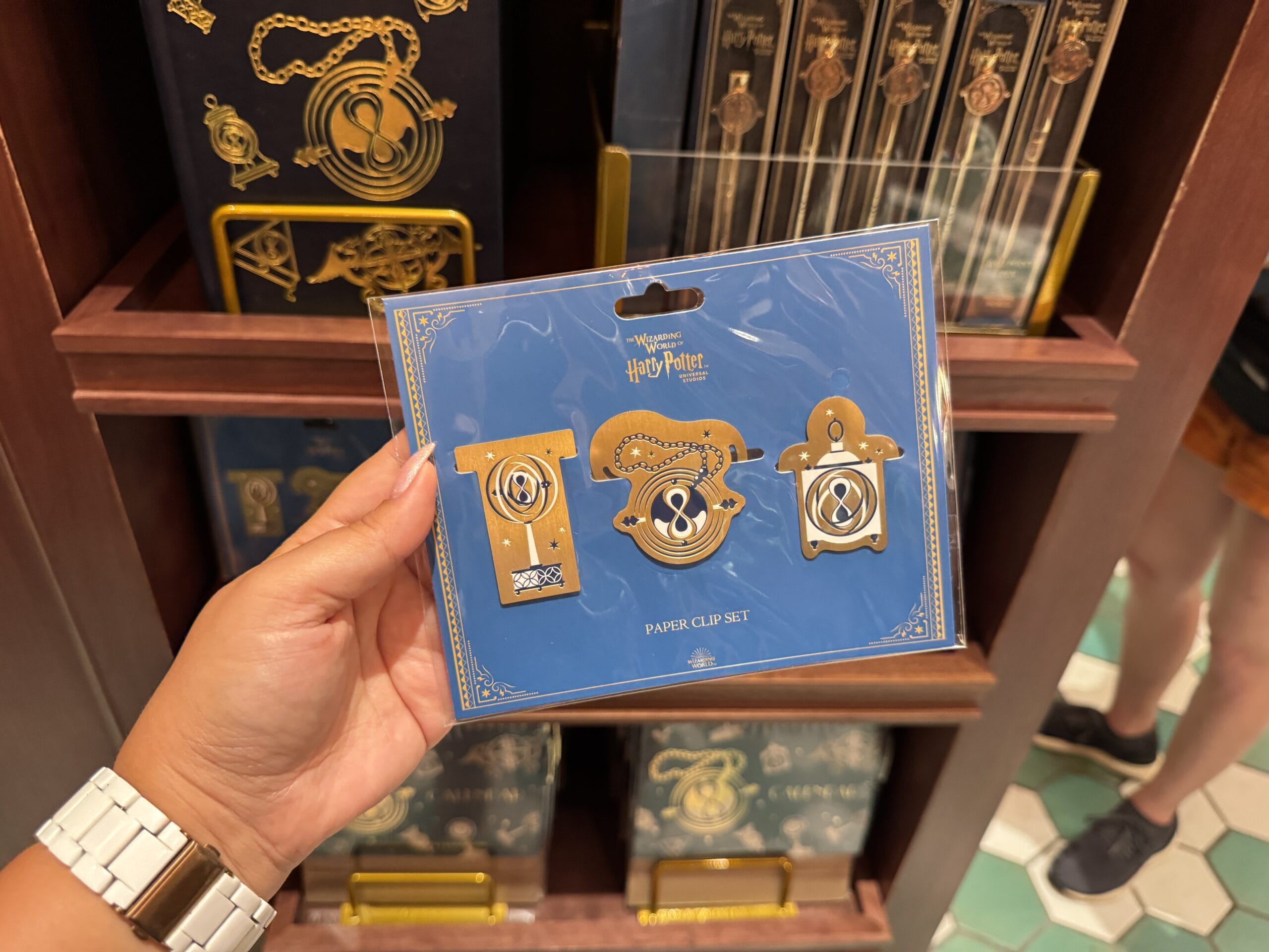 Hand holding a Wizarding World of Harry Potter merchandise paper clip set, shelves stocked in the Epic Universe store.