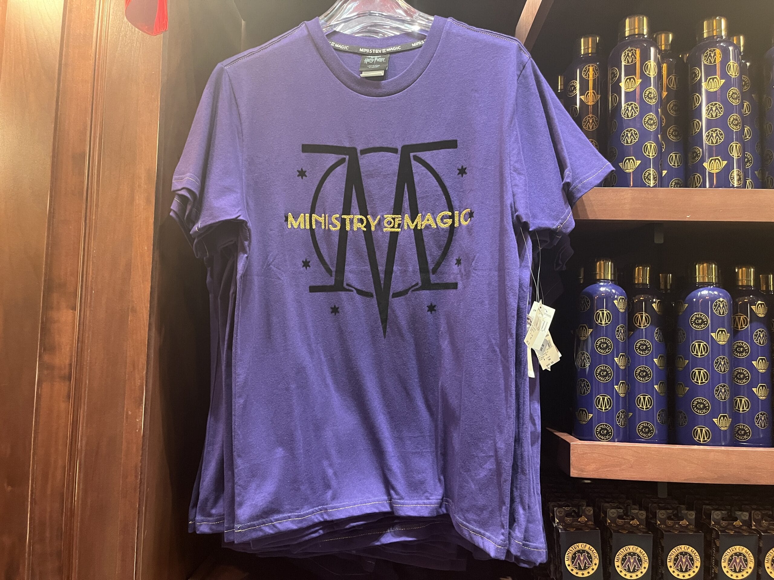 A purple "Ministry of Magic" T-shirt, perfect Wizarding World of Harry Potter merchandise, hangs by matching bottles on display.