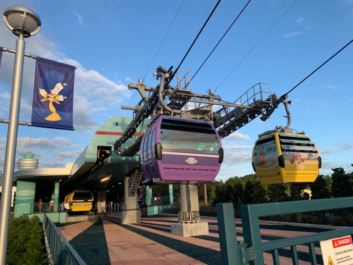 Colorful gondolas approach Disney's Skyliner station, offering views near the Hollywood Studios Entrance under a clear sky.