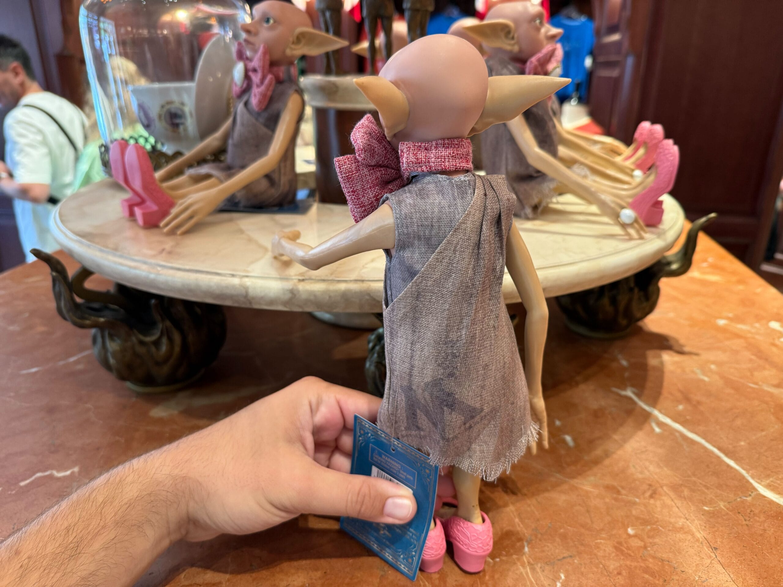 A hand holds a Dobby doll from The Wizarding World of Harry Potter, displayed on a round marble table.