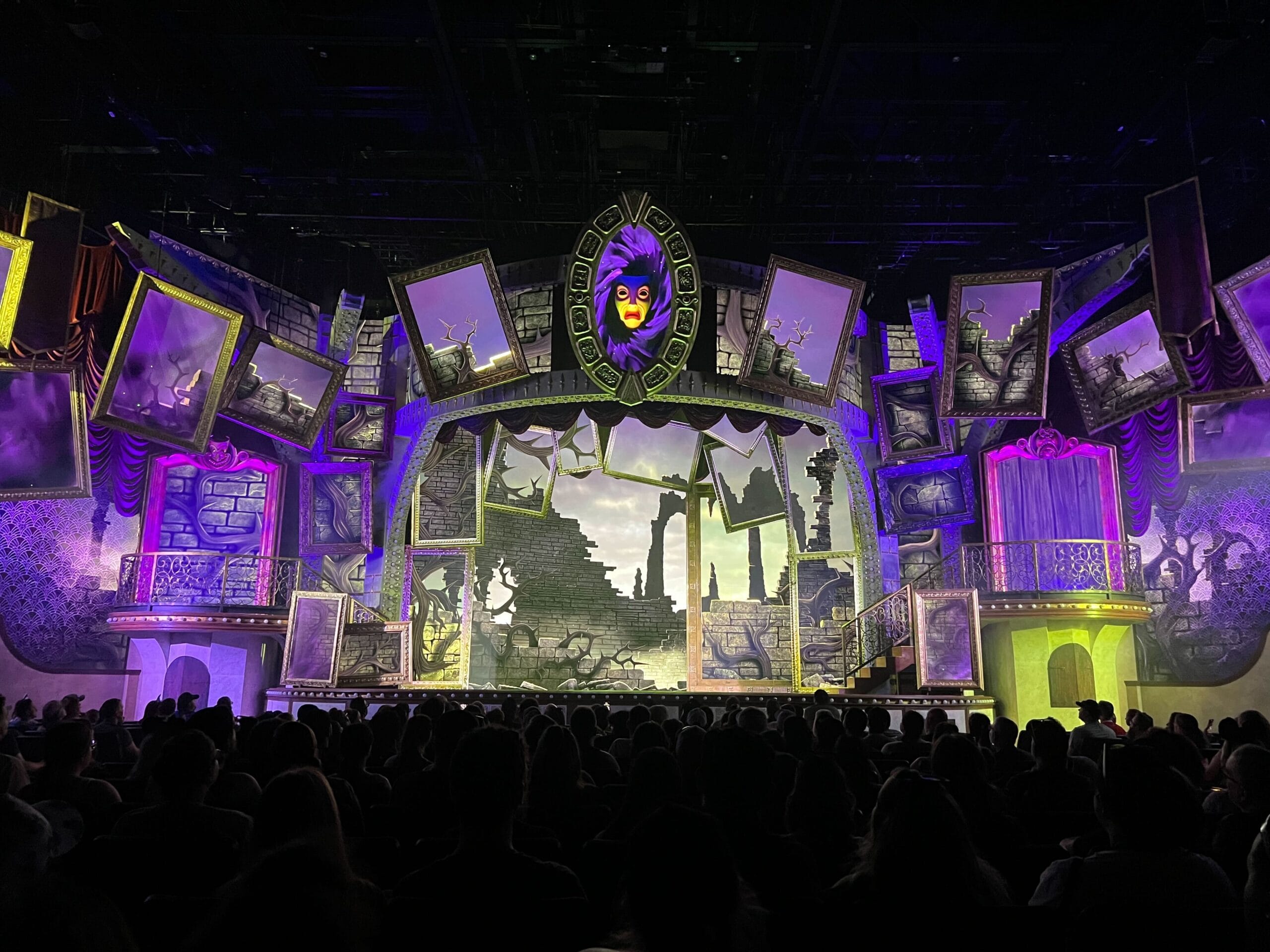 A theater stage with an unfairly ever after fantasy set, crooked frames, a magic mirror, and a ruined castle backdrop.