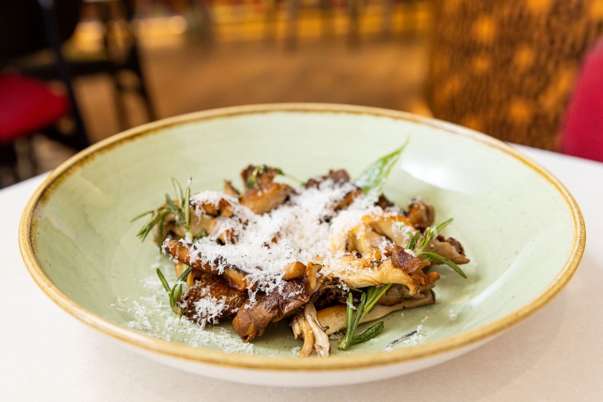 A plate of sautéed mushrooms garnished with grated cheese and fresh herbs on a light green dish.