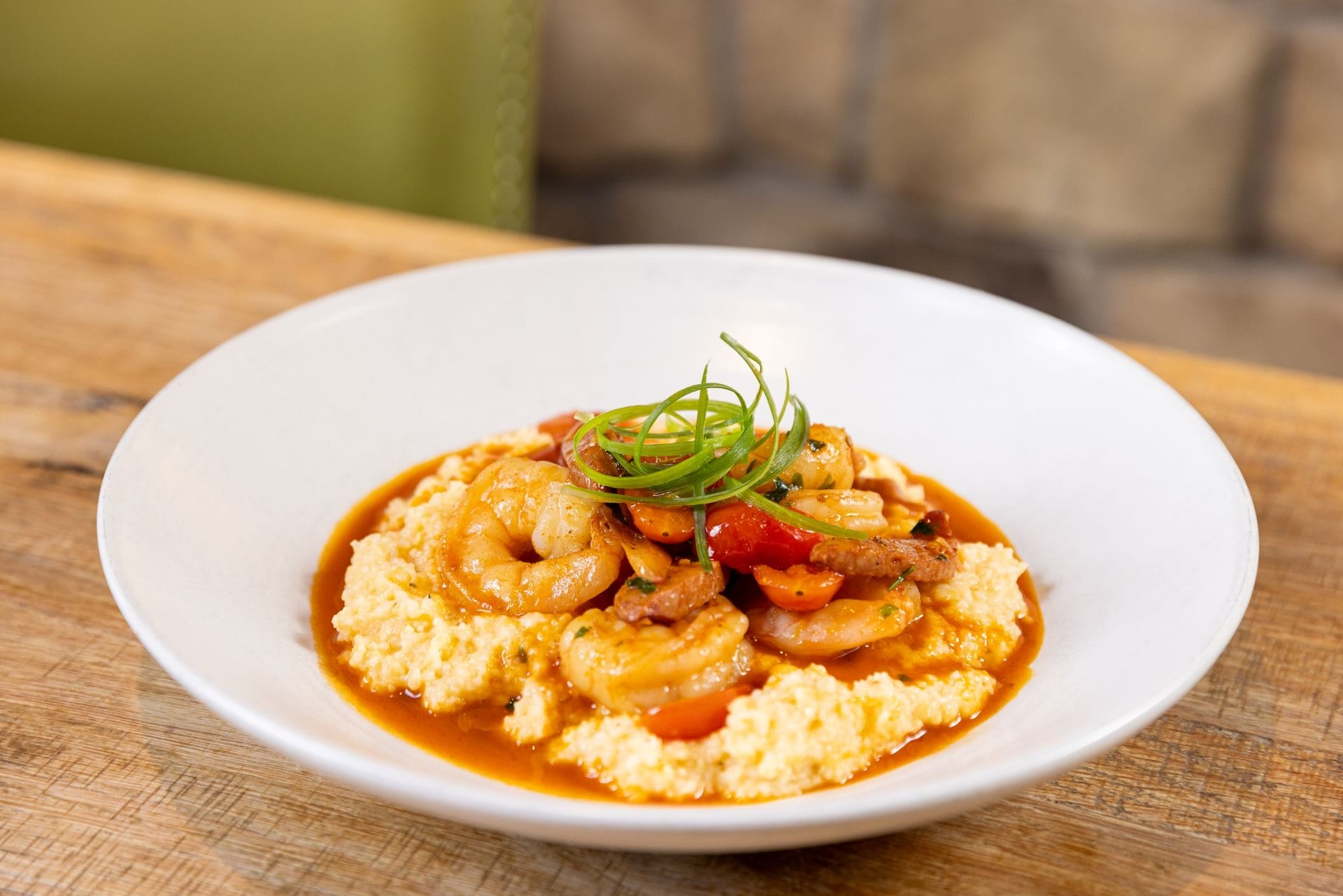 A white bowl of shrimp and tomato stew served over creamy grits, garnished with sliced green onions.
