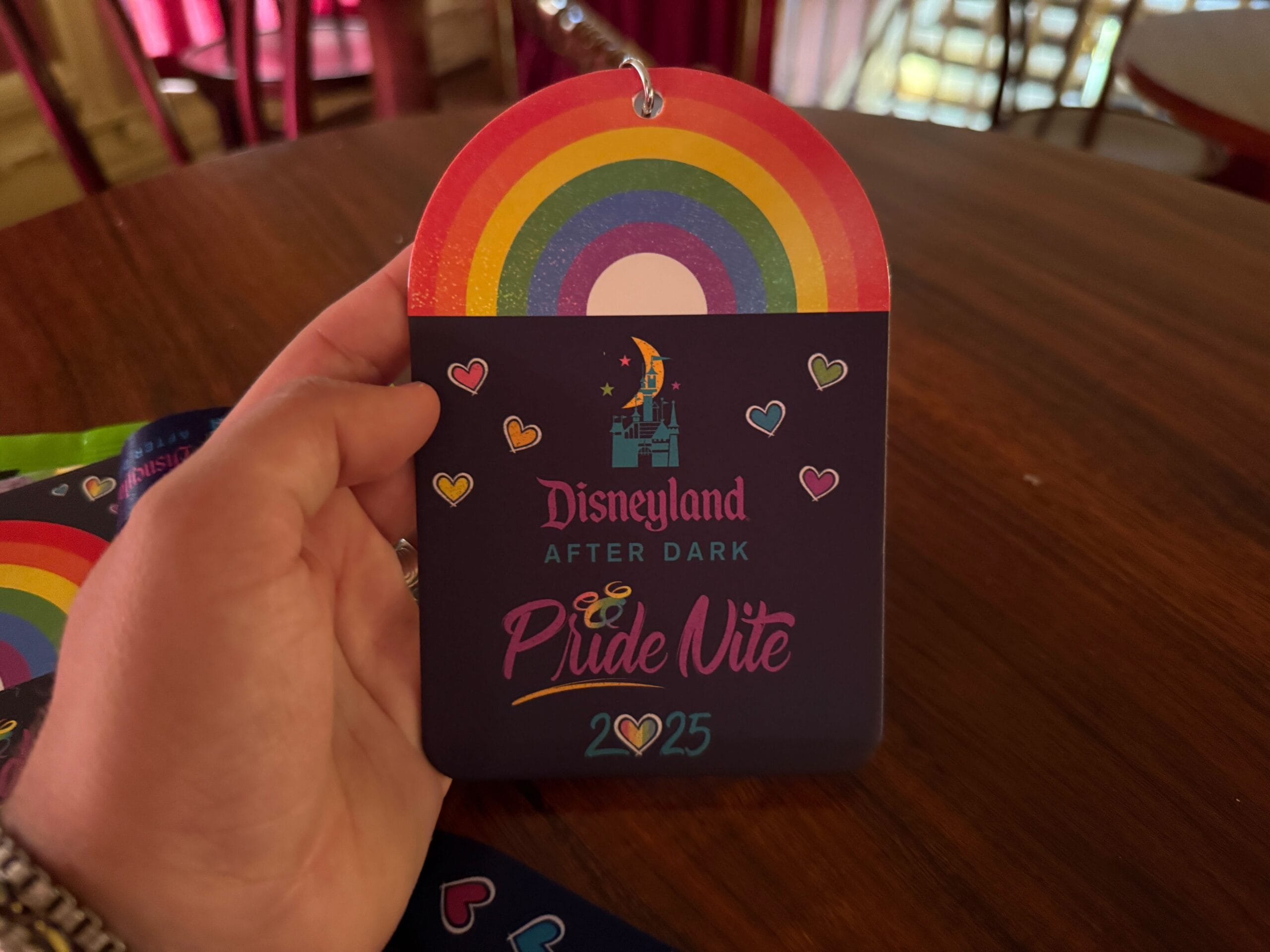 A hand holds a Disneyland Pride Nite 2025 pass with rainbow and heart designs.