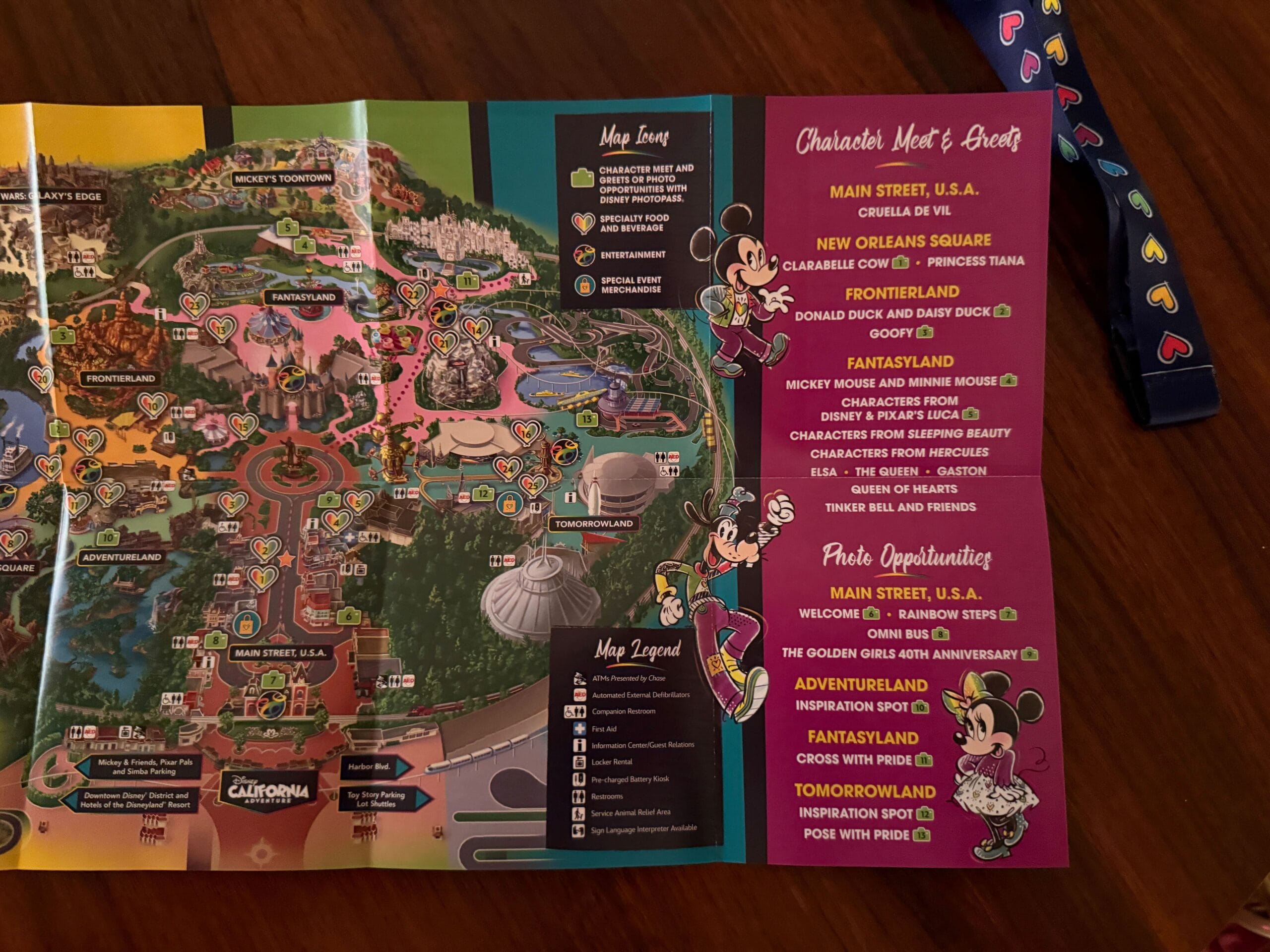 Disneyland Pride Nite credential, 2025 map, and character schedule on a table with a heart-adorned navy lanyard.