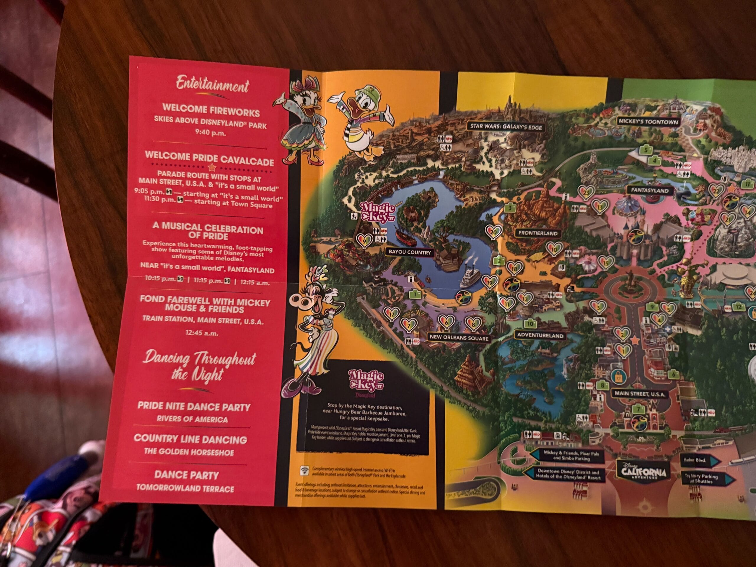 A Pride Night map on a table, with a red sidebar listing Disneyland Pride Nite events and dance parties.
