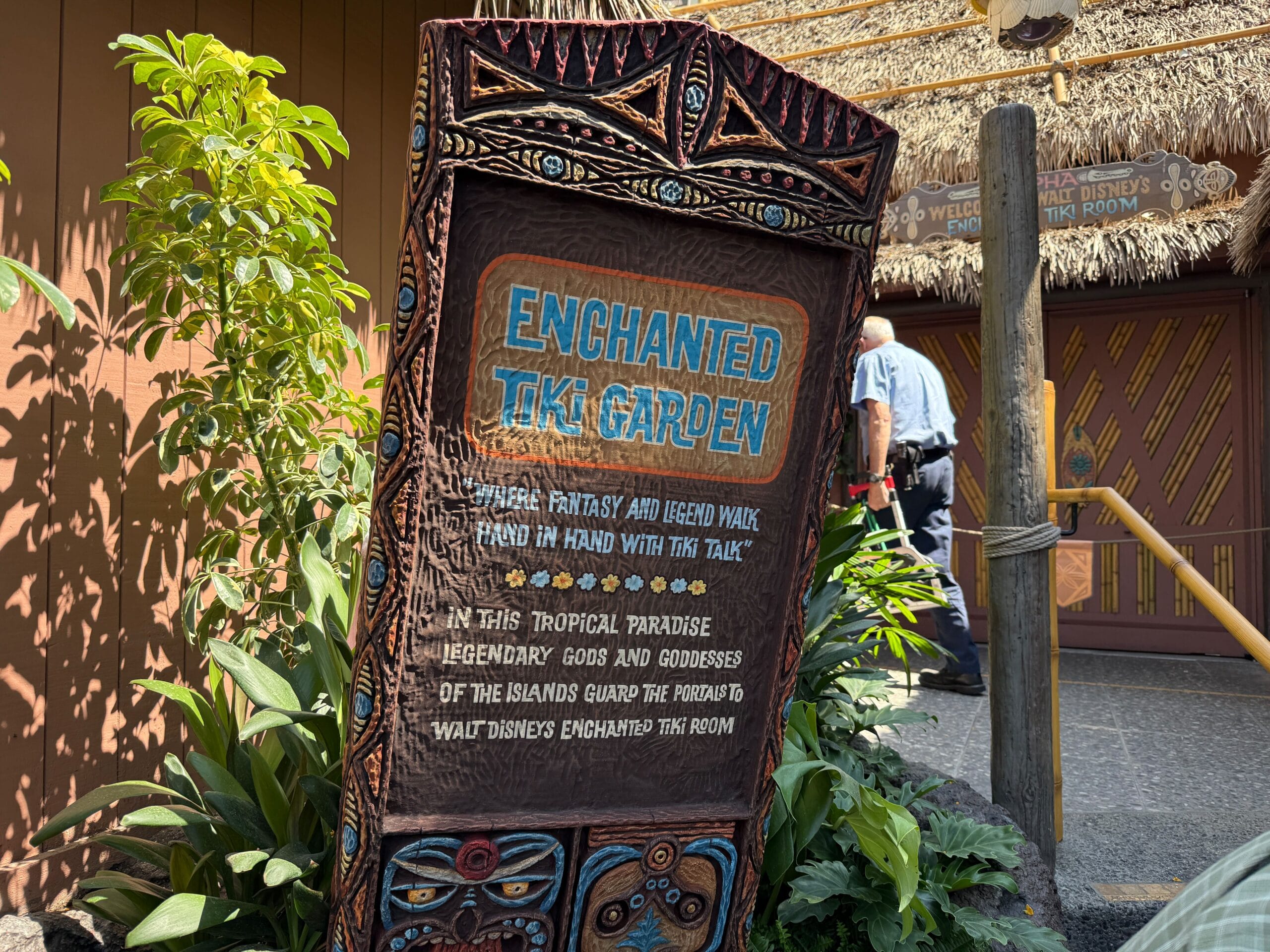 A carved wooden sign for Enchanted Tiki Garden welcomes guests outside Disneyland’s lush, tropical-themed building.