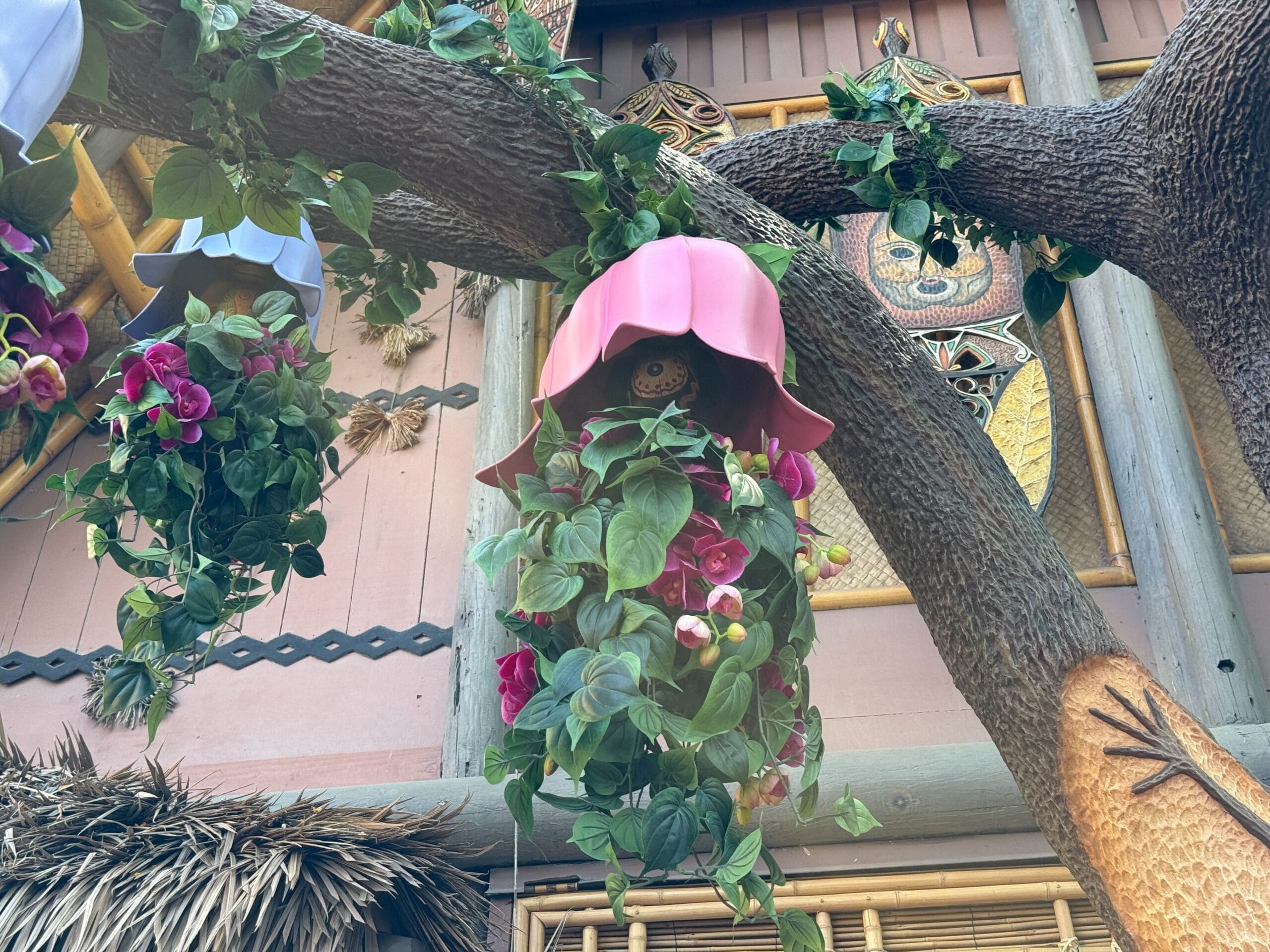 Pink flower-shaped lantern with leafy vines in the Enchanted Tiki Garden near Walt Disney’s Enchanted Tiki Room facade.