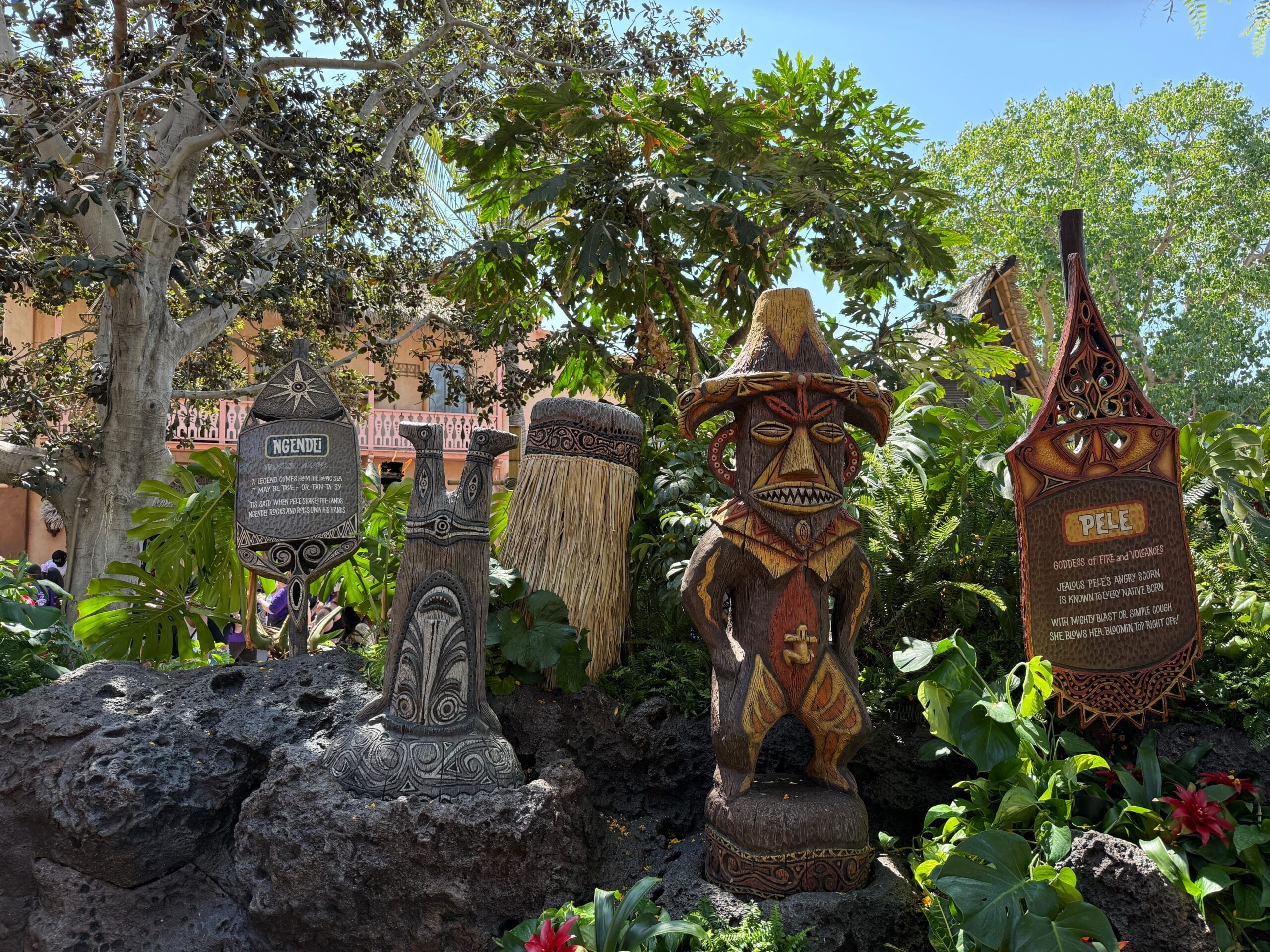 Four Polynesian tiki statues and signs enliven the Enchanted Tiki Garden’s lush greenery at Walt Disney’s Enchanted Tiki Room.