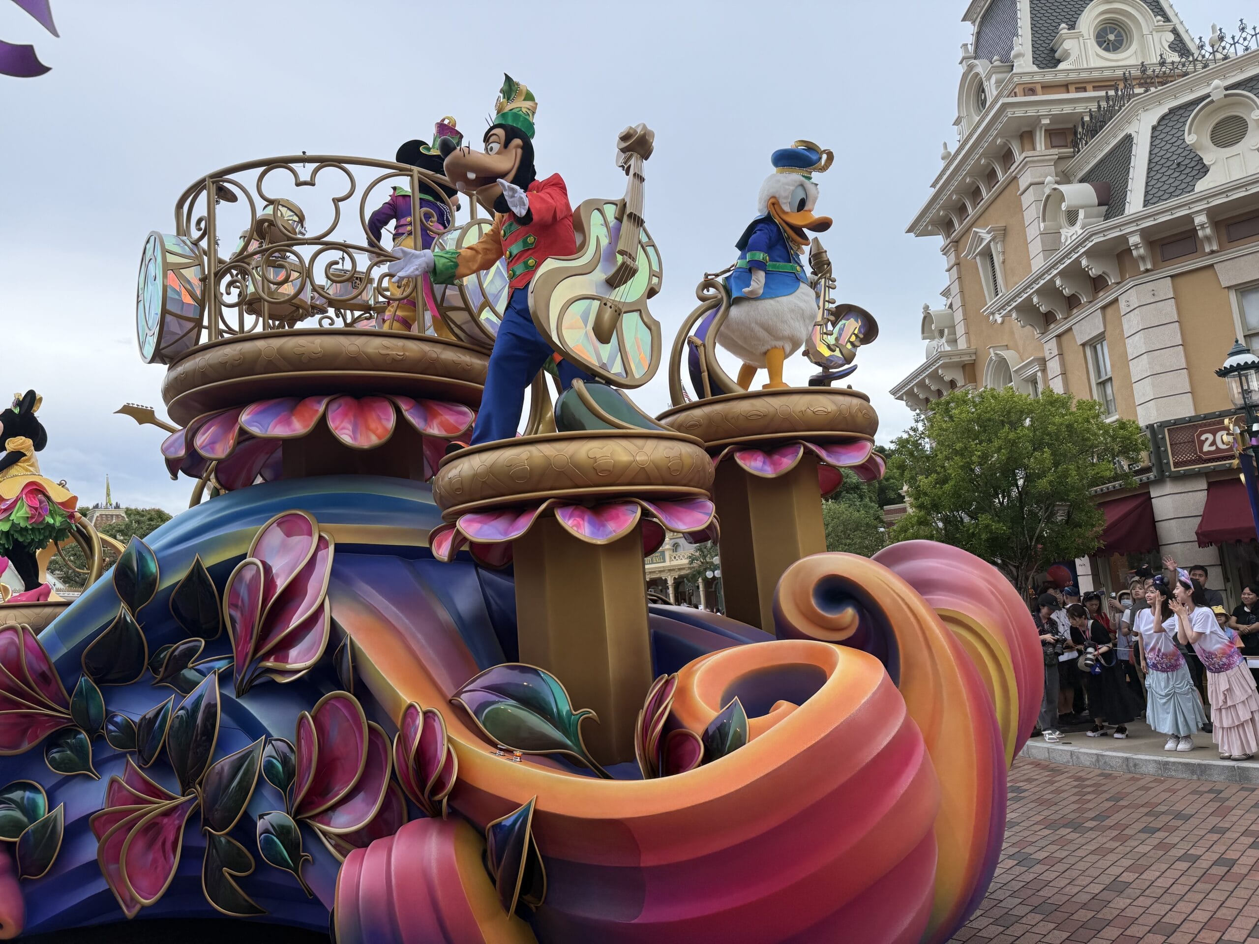 Colorful Friendtastic Parade float at Hong Kong Disneyland with Goofy and Donald Duck playing instruments, crowds watching nearby.
