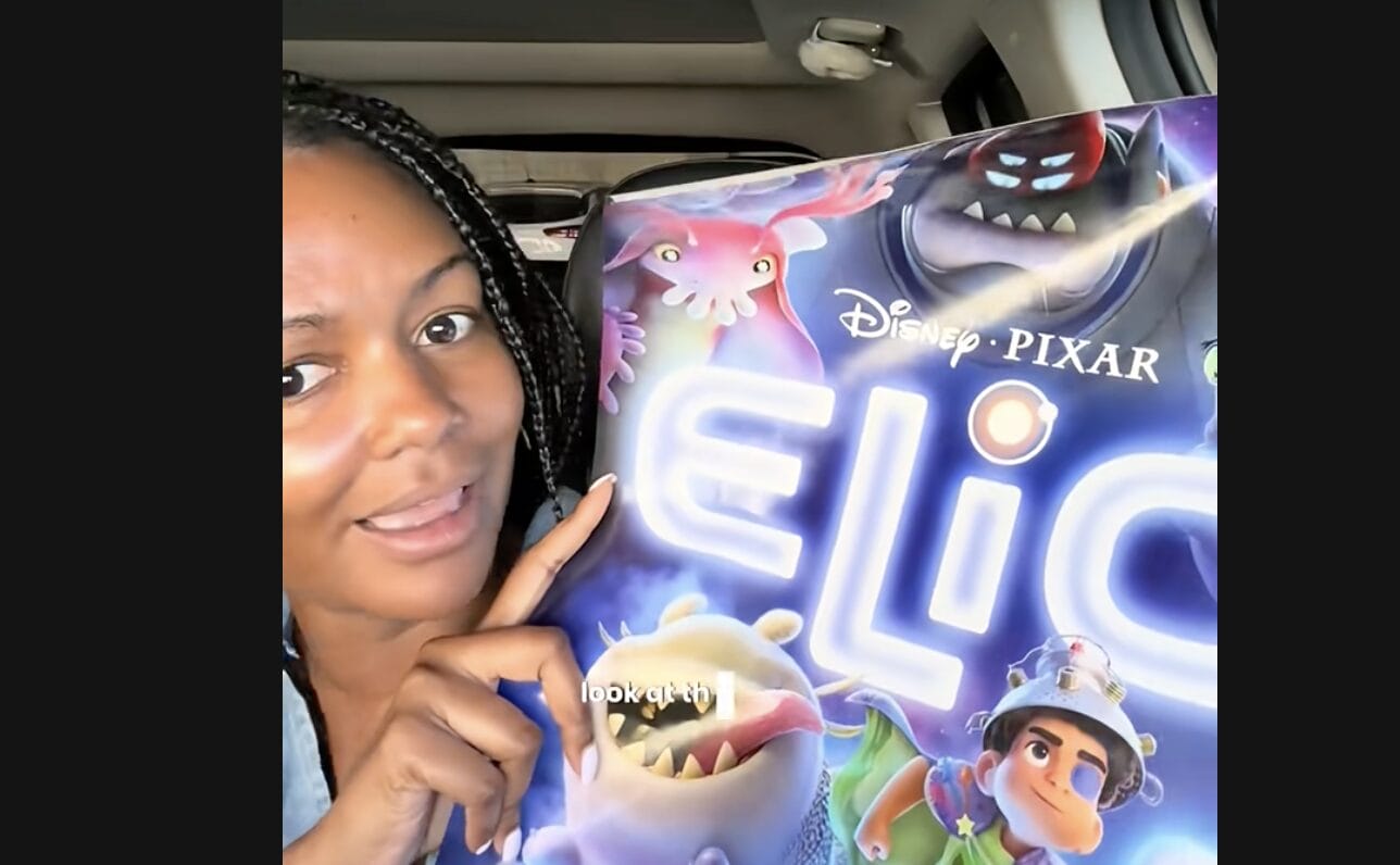 Woman smiling and pointing at a Pixar "Elio" poster featuring animated characters from the original film.