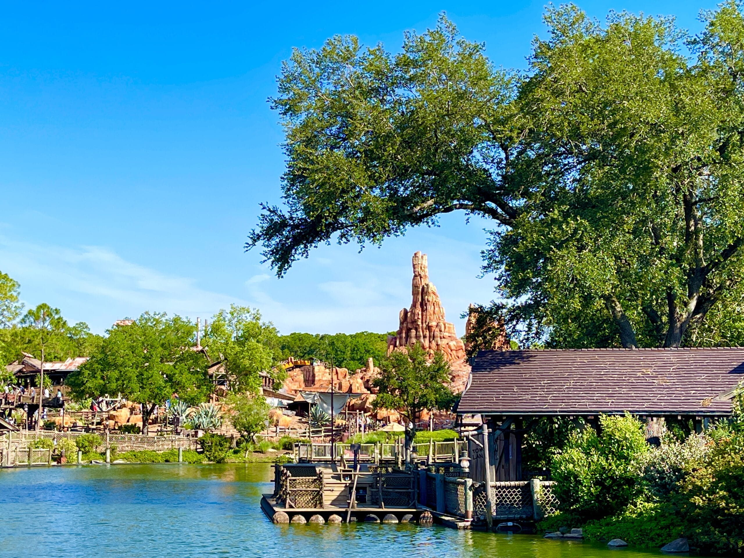 A rustic wooden dock on Tom Sawyer Island sits by a lake, backed by red rocks under a clear blue sky ahead of tom sawyer island closing