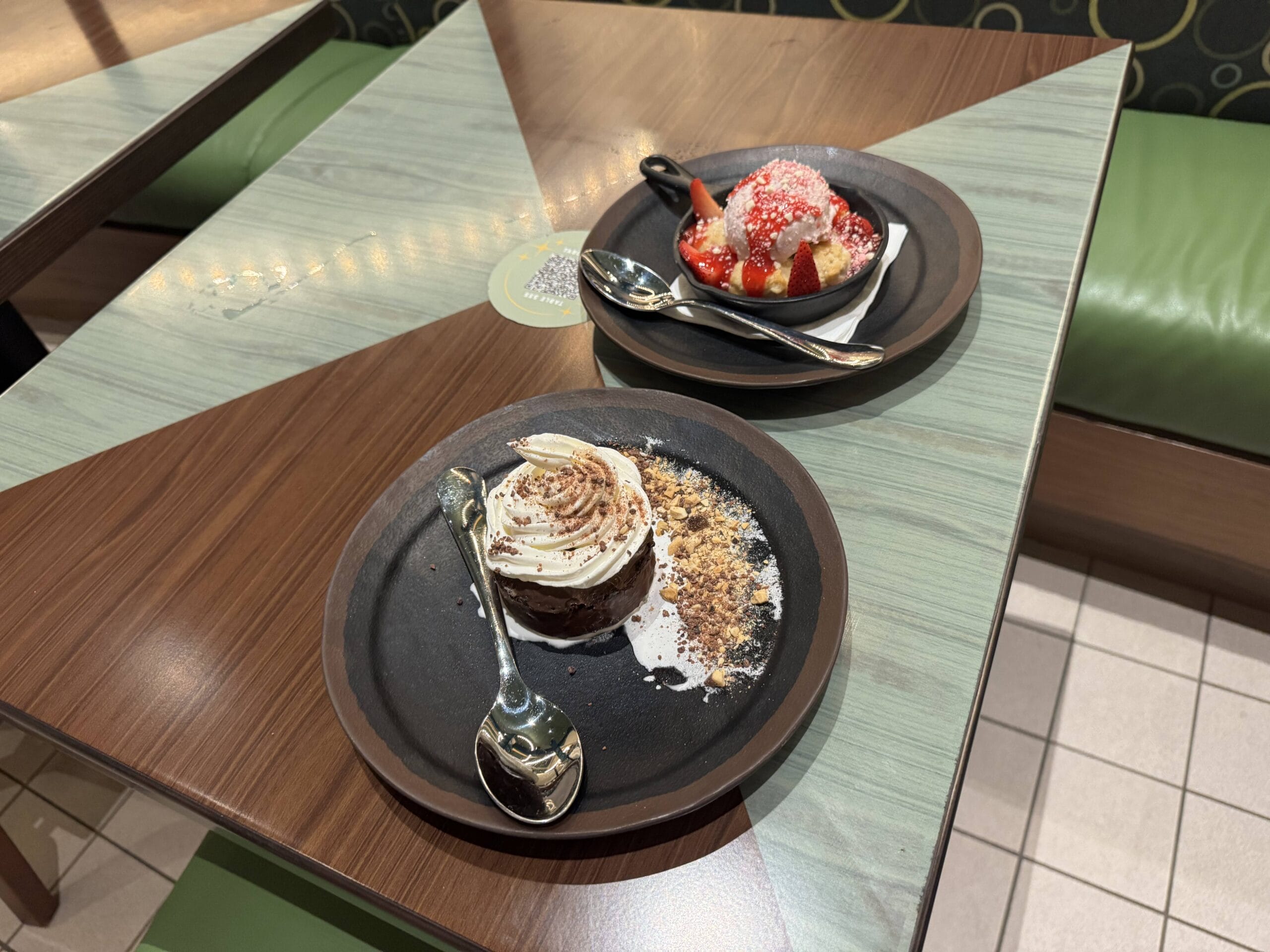 Two dessert plates at Meteor Astropub: chocolate cake and strawberries with cream, ready at Epic Universe. Spoons beside each.