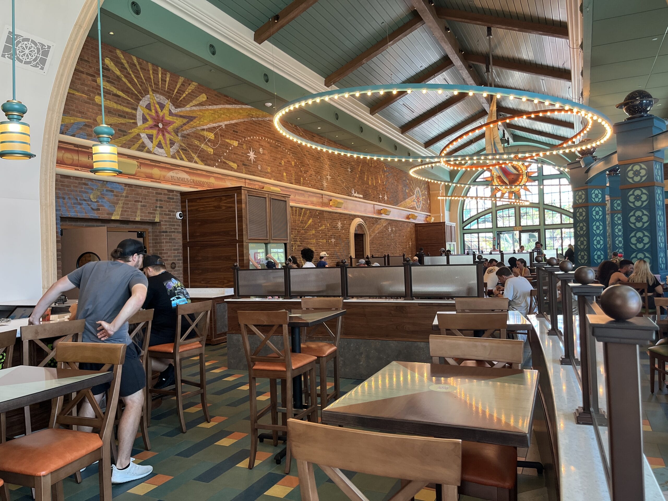 Spacious Meteor Astropub with high ceilings, mural walls, hanging lights, and diners at wooden tables and chairs.