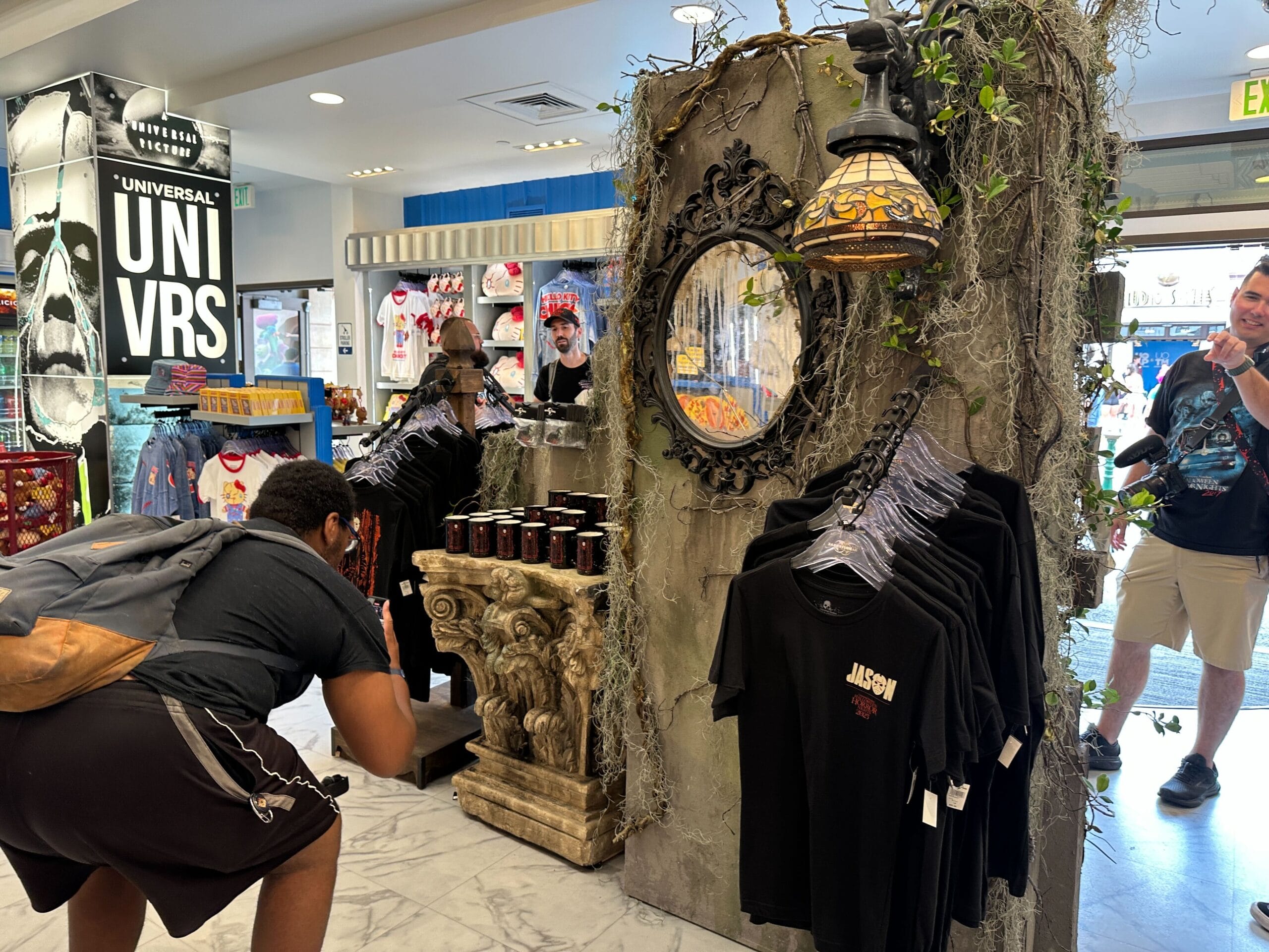 A person snaps a photo of Friday the 13th shirts in a horror-themed Universal Studios Florida store display.