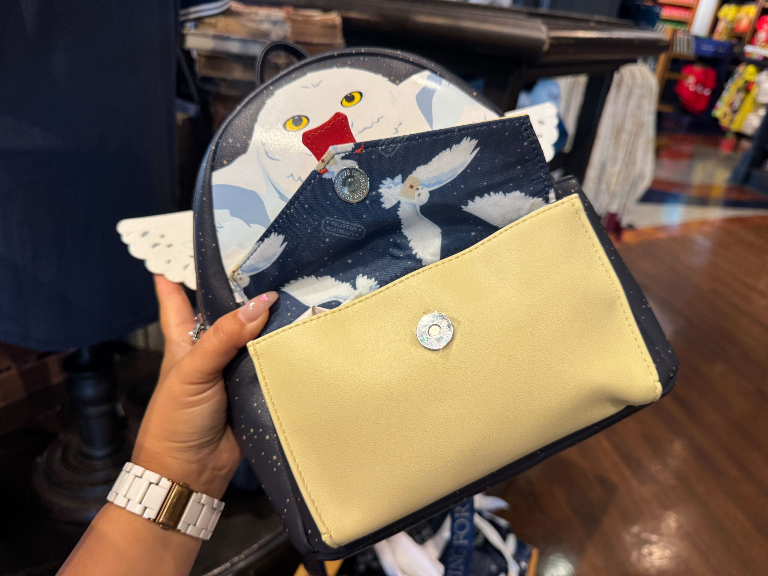 A hand holds an opened handbag with a white Hedwig owl design, wings spread, revealing a matching pouch inside.