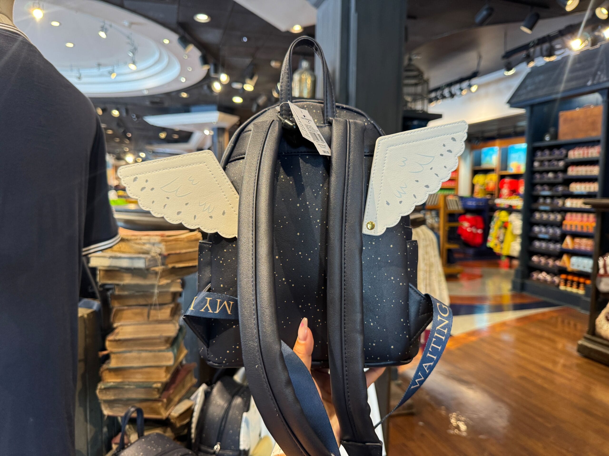 A black backpack with white wings and gold speckles evokes Hedwig, waiting for a letter in a store of Harry Potter merchandise.