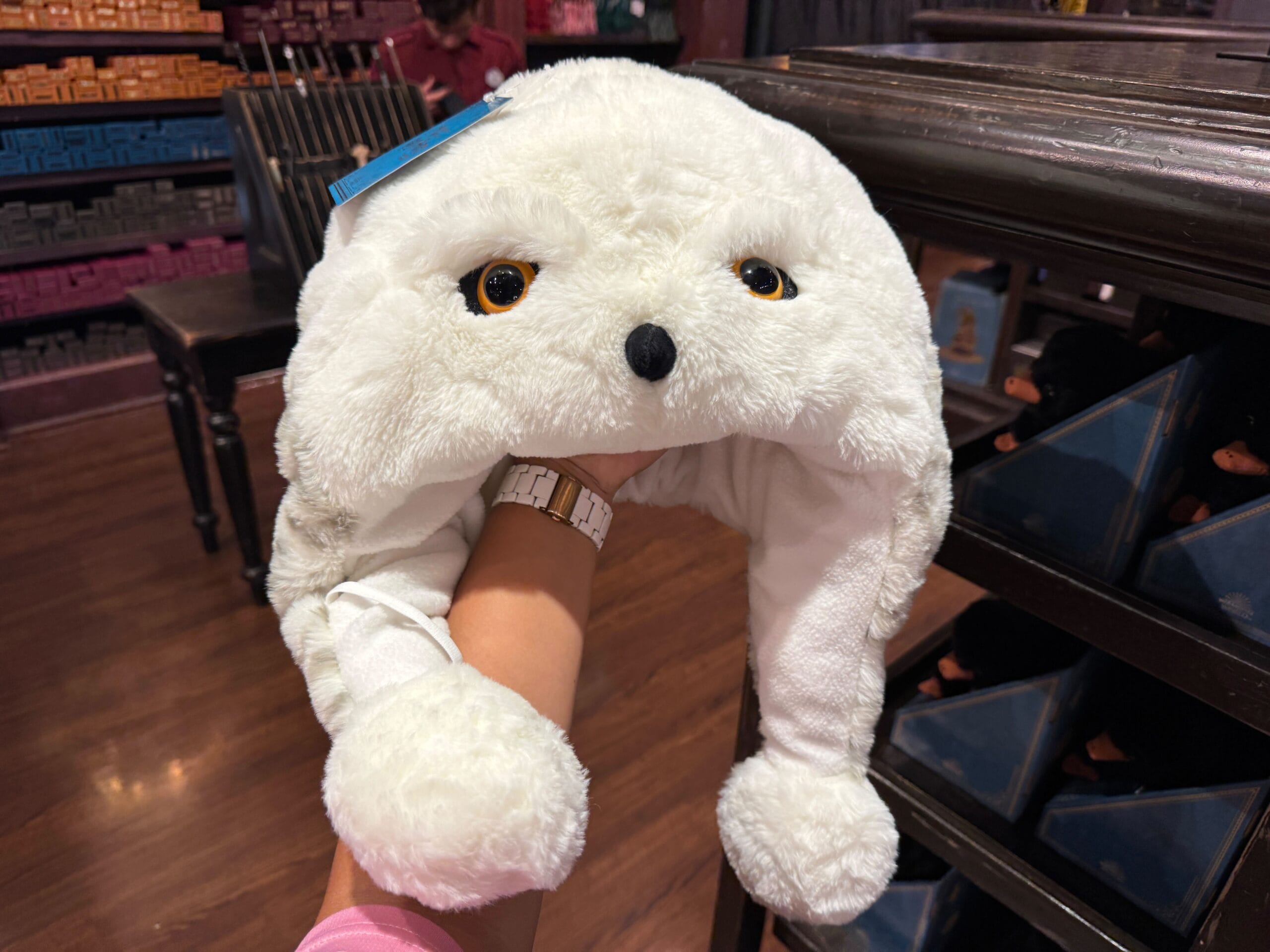 A person holds a Hedwig plush owl hat with black eyes and a beak inside a store.
