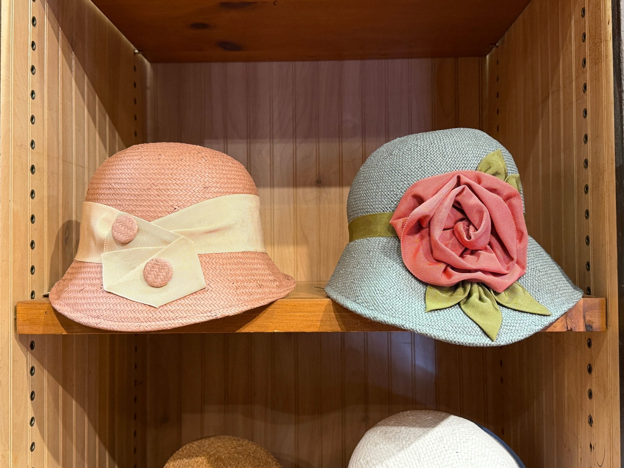 Two vintage-style hats at the Prairie Outpost Hat Shop: one pink with buttons, one blue with a pink flower.