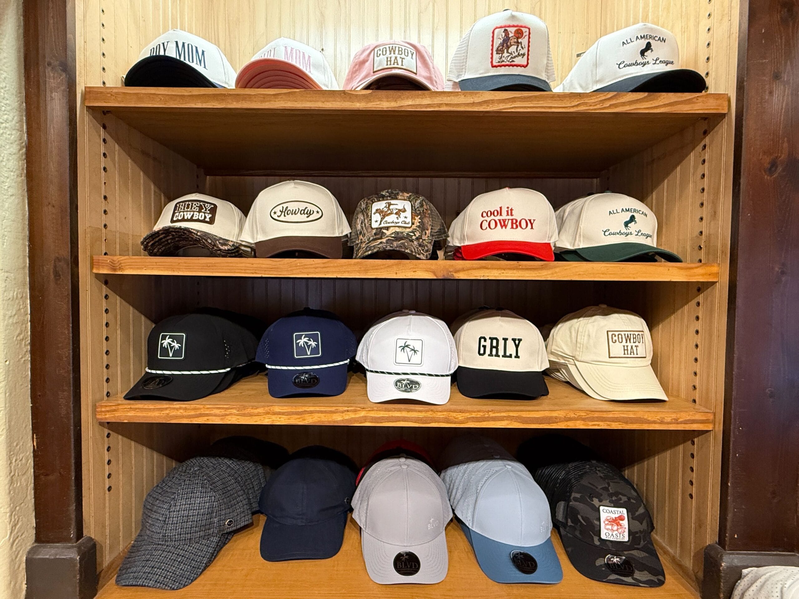Four shelves at Prairie Outpost Hat Shop display cowboy and trucker hats in various colors against a wooden backdrop.