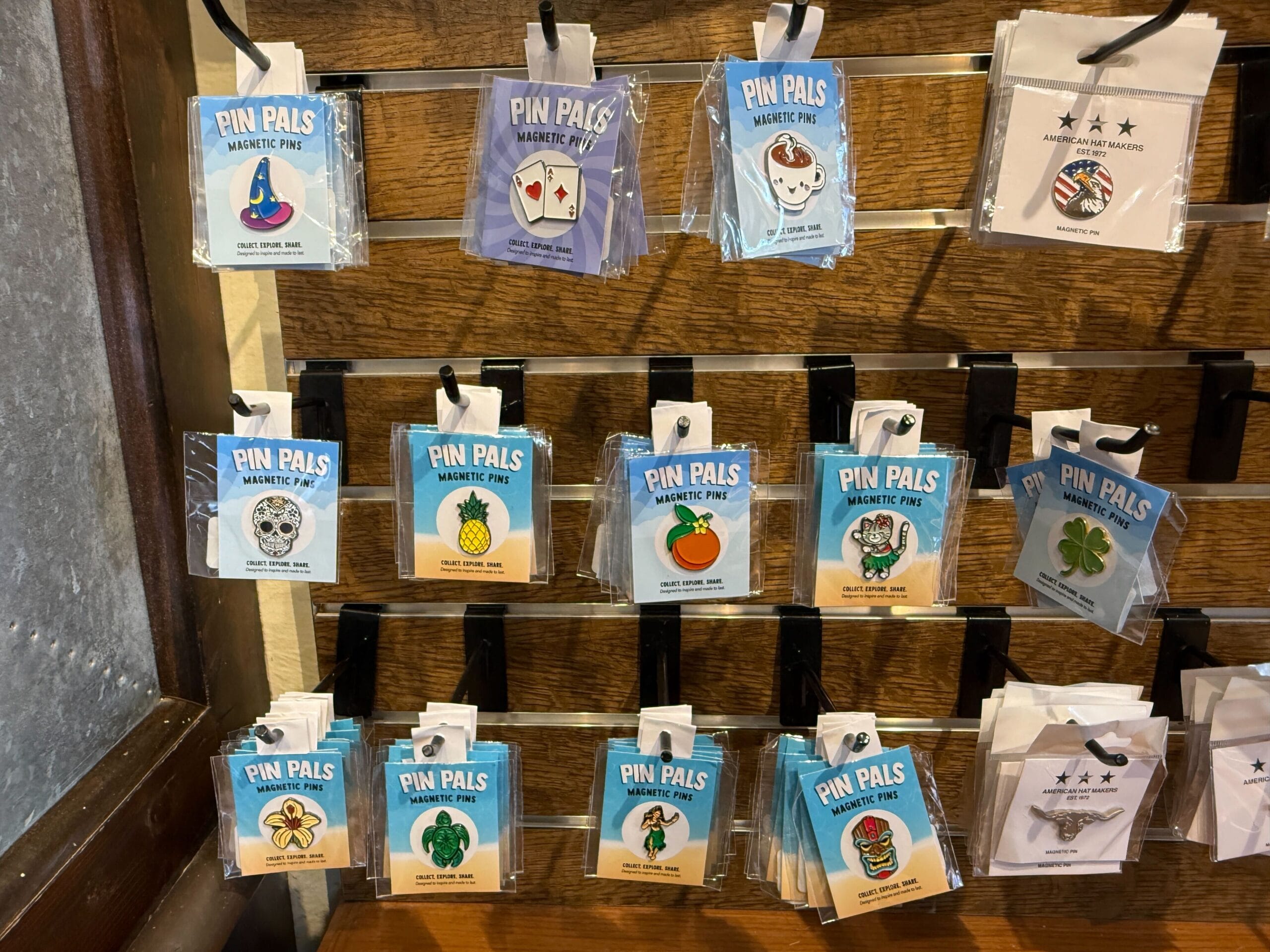 A display of colorful “Pin Pals” magnetic pins at Prairie Outpost features cards, pineapples, and pumpkins on a wooden wall.