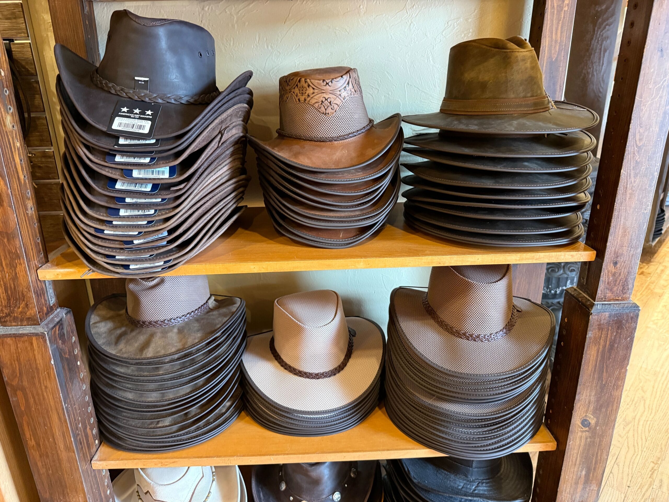 Stacks of brown and tan cowboy hats are neatly arranged on wooden shelves at the Prairie Outpost Hat Shop.