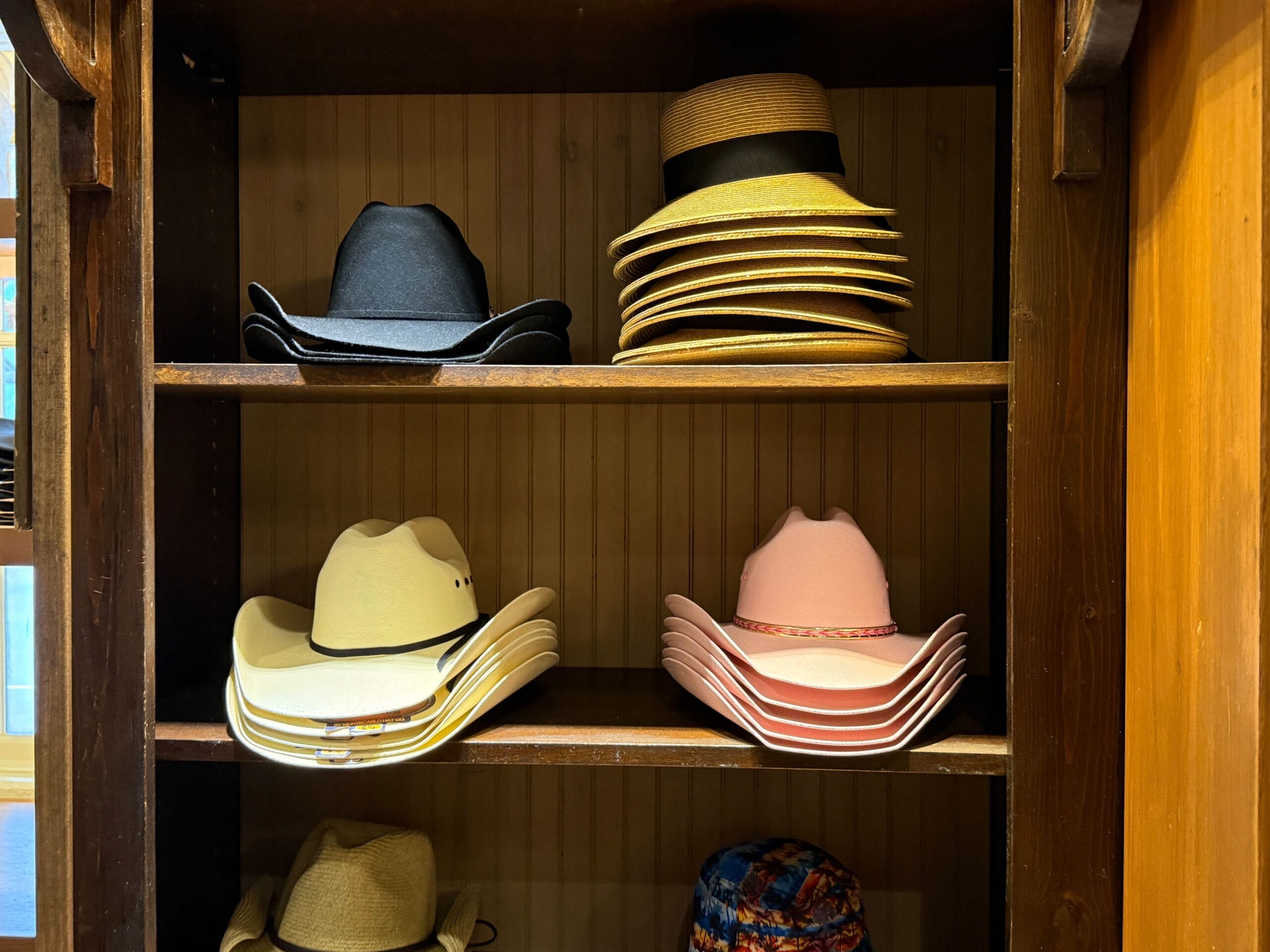 Shelves at Prairie Outpost display black, beige, pink, and brown hats neatly stacked in a wooden cabinet.