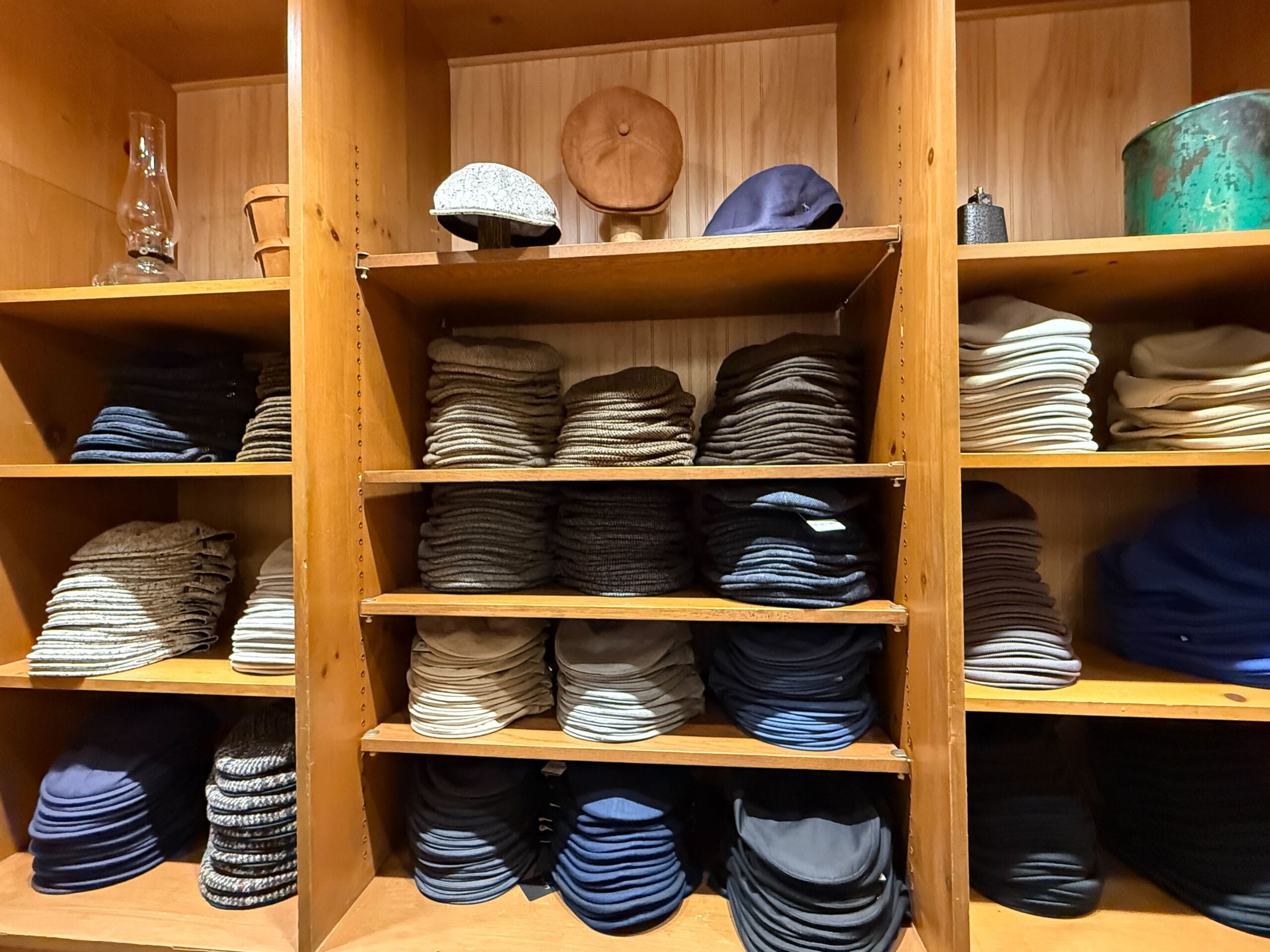 Wooden shelves at the Hat Shop are neatly stacked with various caps and hats in different colors and fabrics.