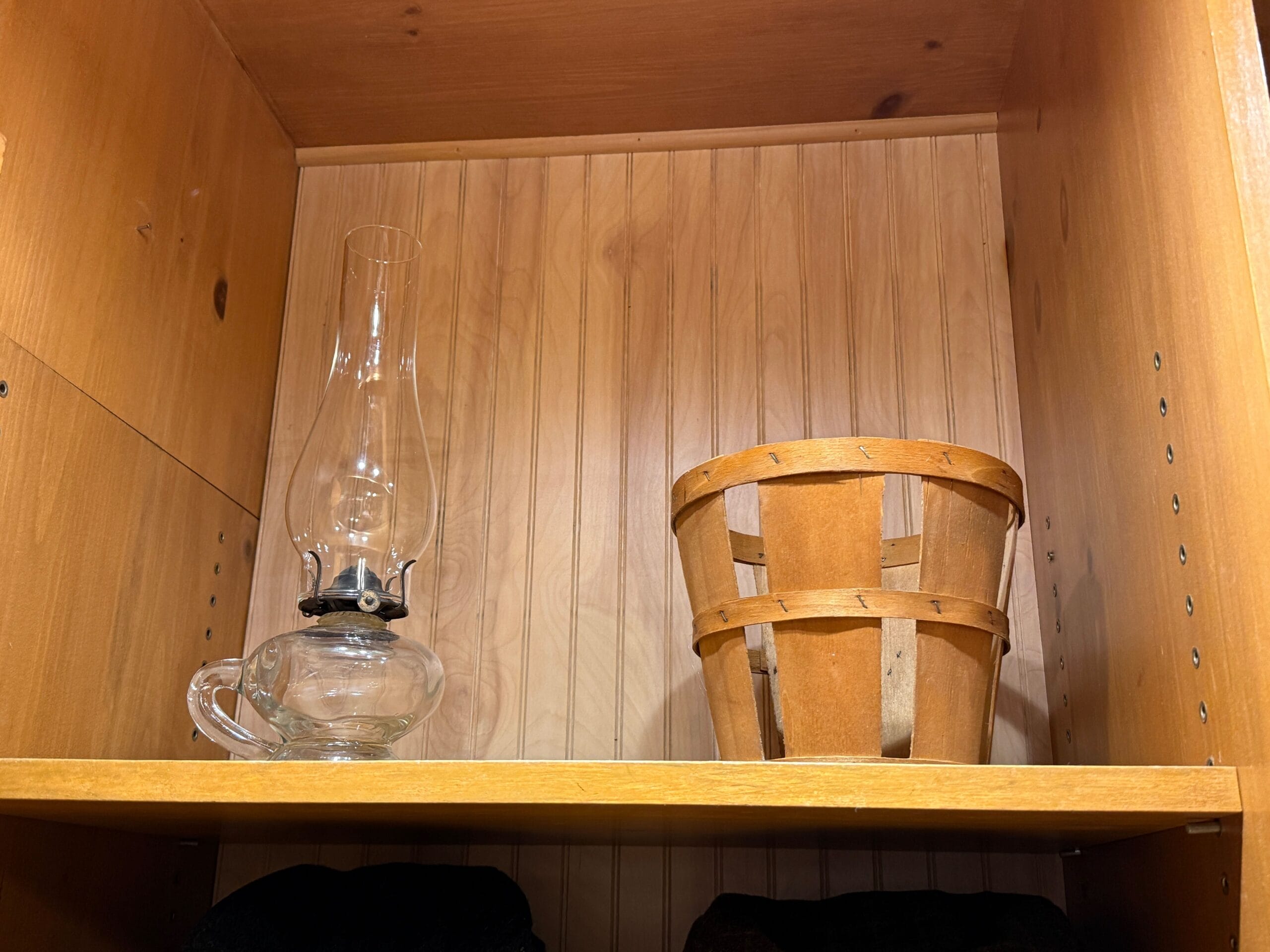 A glass oil lamp and small wooden basket sit on a wooden shelf at Prairie Outpost in Magic Kingdom.