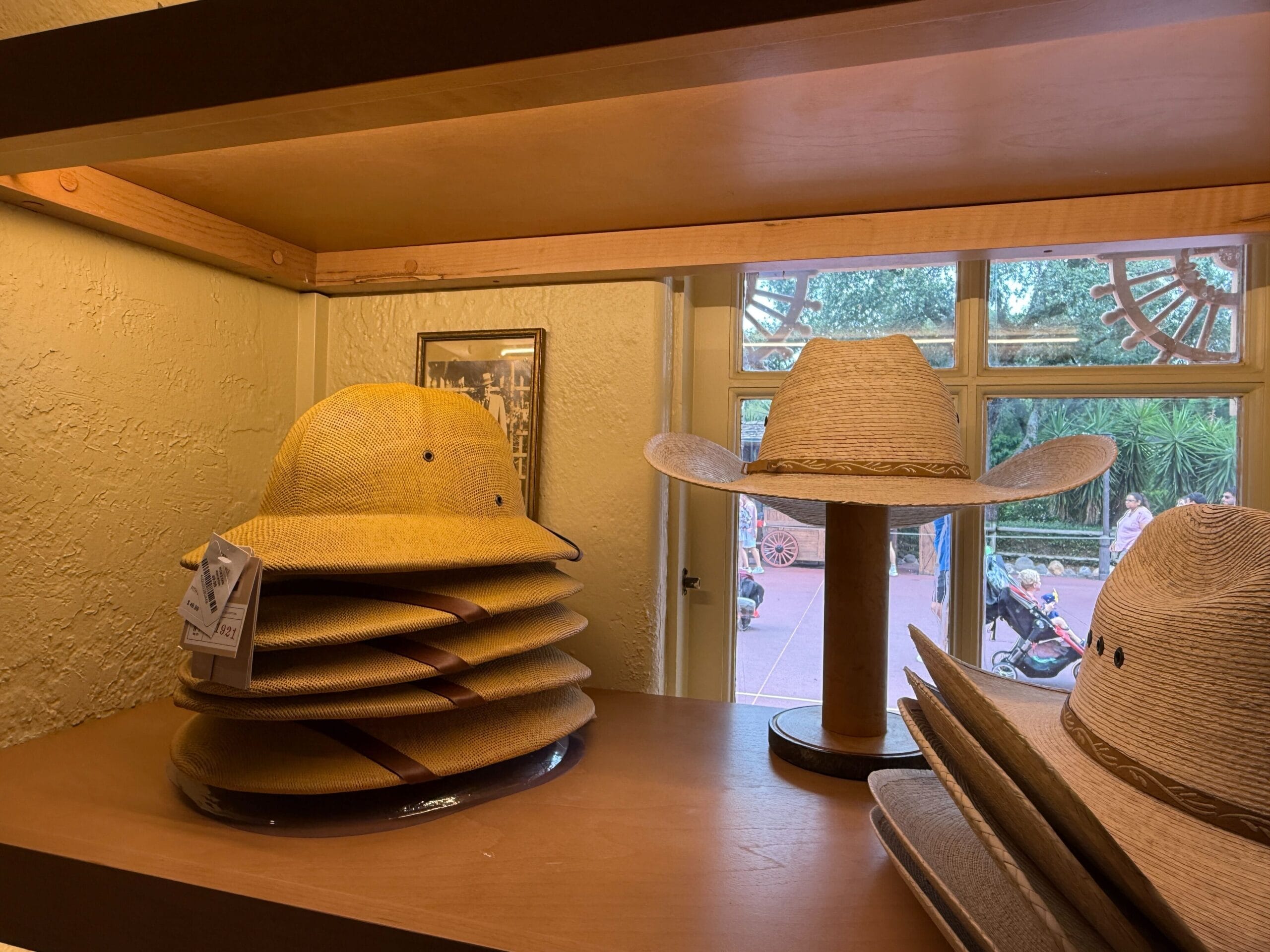 A stack of yellow safari hats and a straw sombrero are displayed at Prairie Outpost in Magic Kingdom near a window.