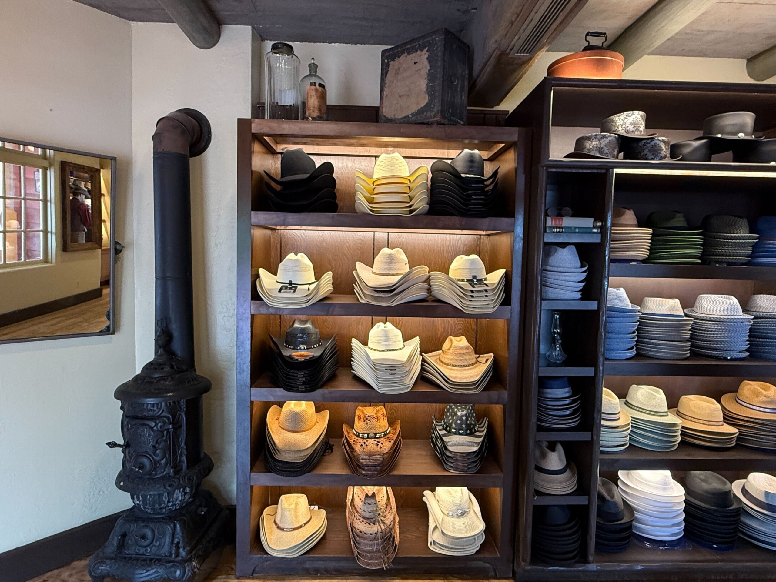 Shelves at Prairie Outpost display cowboy hats and fedoras beside a vintage stove in this rustic Hat Shop.