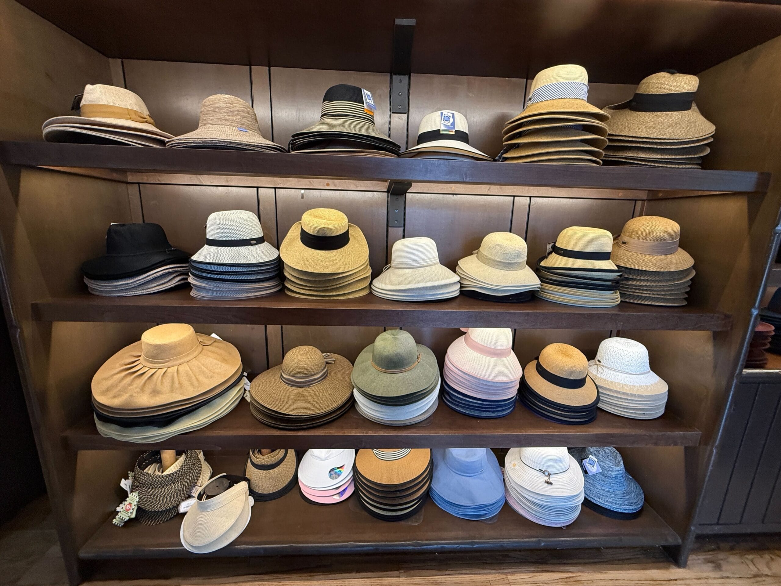 Shelves in the Prairie Outpost Hat Shop display straw and fabric hats of all shapes, sizes, and colors in a wooden cabinet.