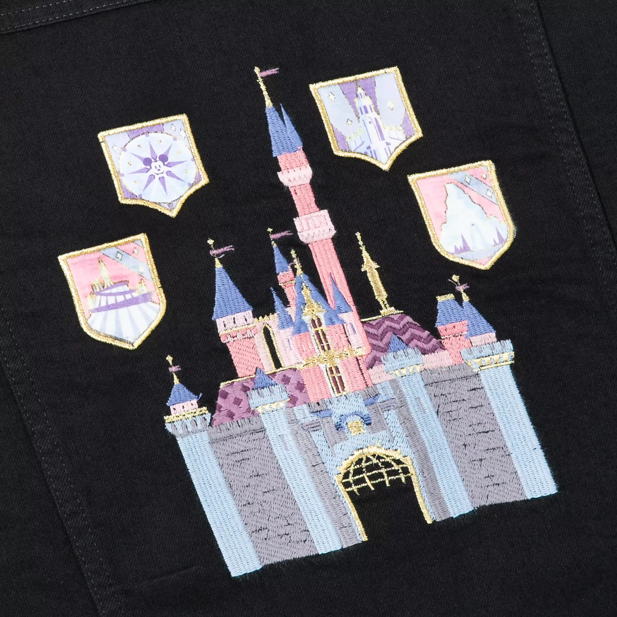 Embroidered pastel castle with four themed shields on a black fabric background.