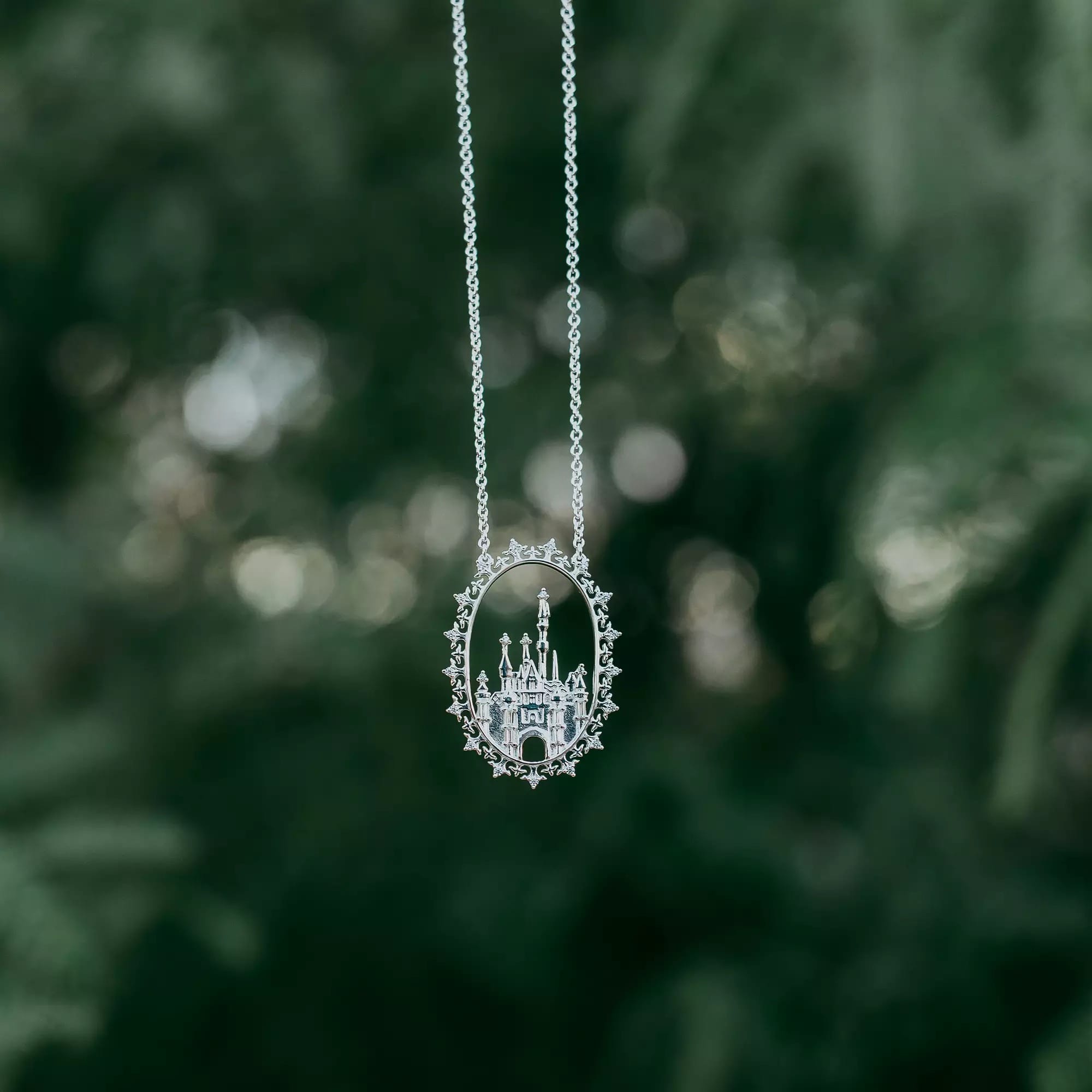 Silver necklace with a detailed castle pendant, hanging against a blurred green natural background.
