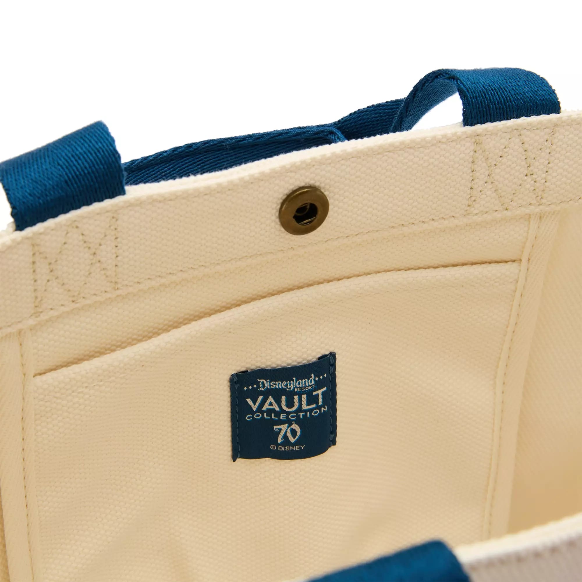 Close-up of a cream tote bag with blue handles and a "Disneyland Vault Collection 70" label inside.