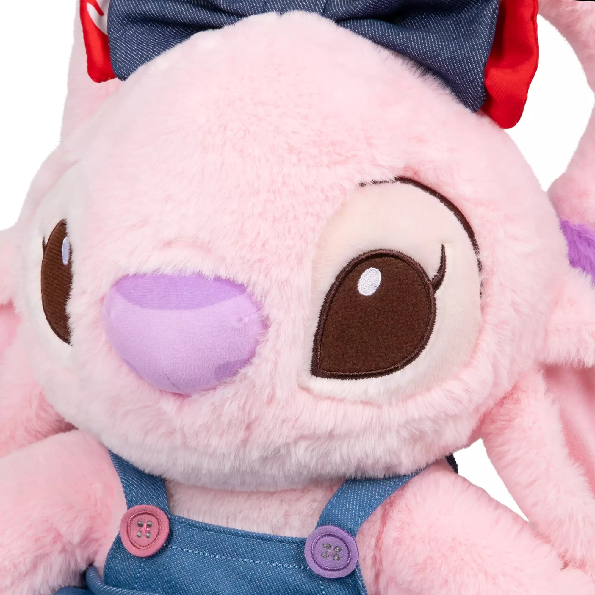 A close-up of a pink Angel plush with big brown eyes, denim overalls, and a blue bow from Disney Store China.