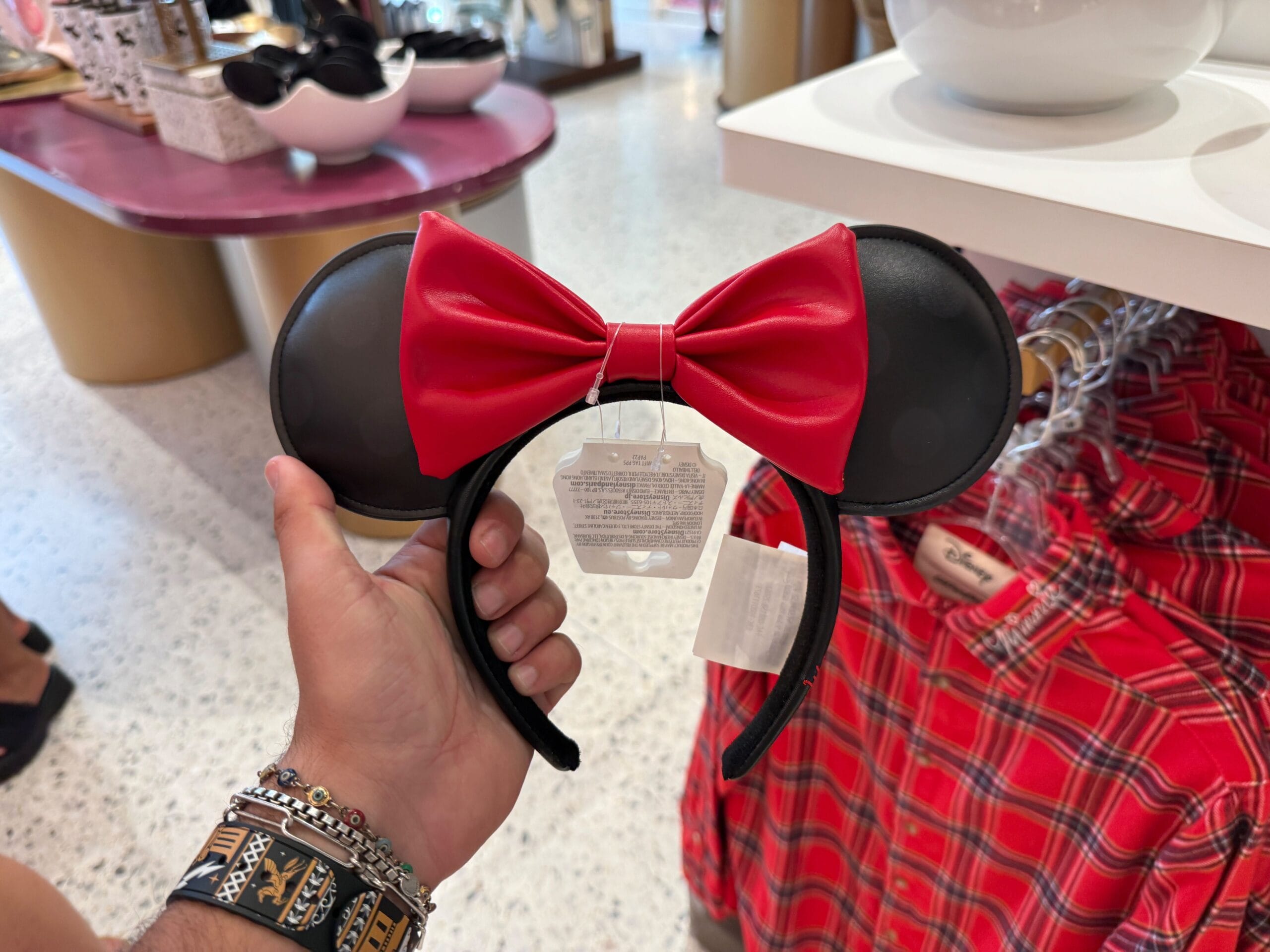 A hand holds up a Minnie Mouse ears headband with a red bow at the Disneyland Resort store.