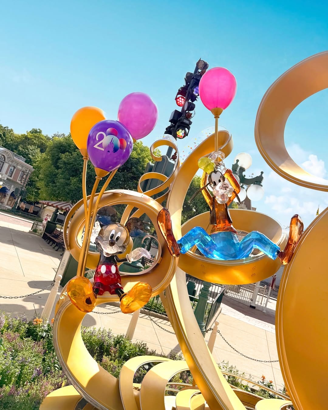 Colorful statues of Mickey and Goofy holding balloons on a yellow spiral structure in an outdoor park.