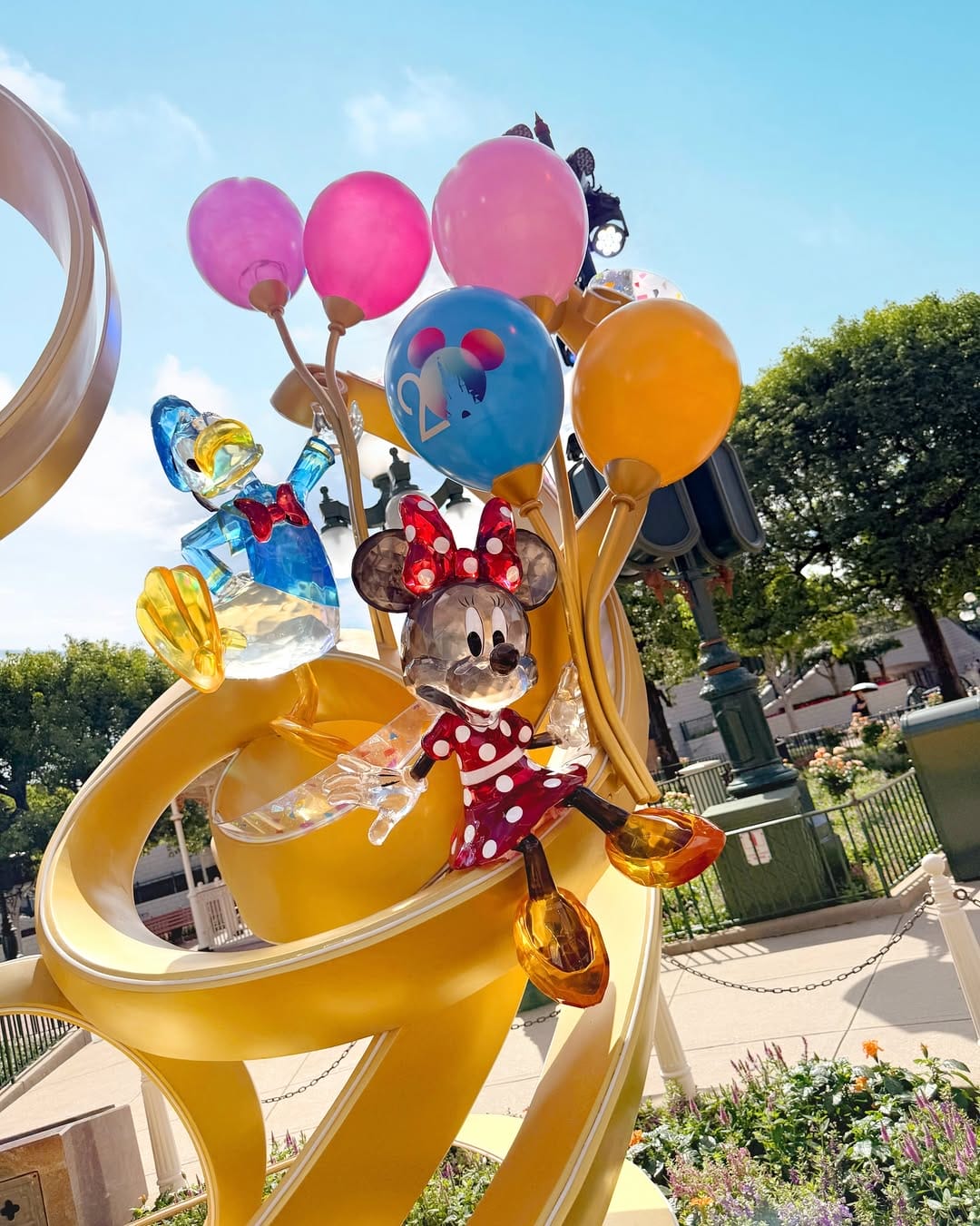 Colorful sculpture of Minnie Mouse holding balloons, with Donald Duck nearby, displayed outdoors on a sunny day.