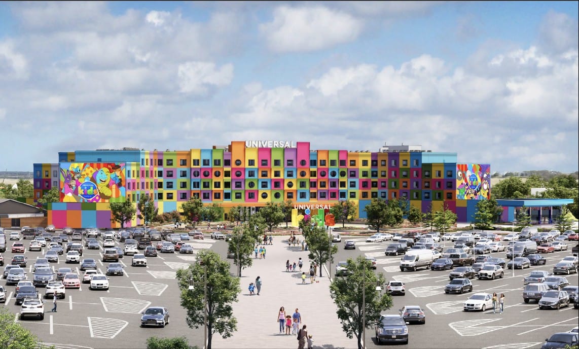 Colorful hotel with "Universal Kids Resort" sign, mural art, and parked cars in a large lot under a partly cloudy sky.