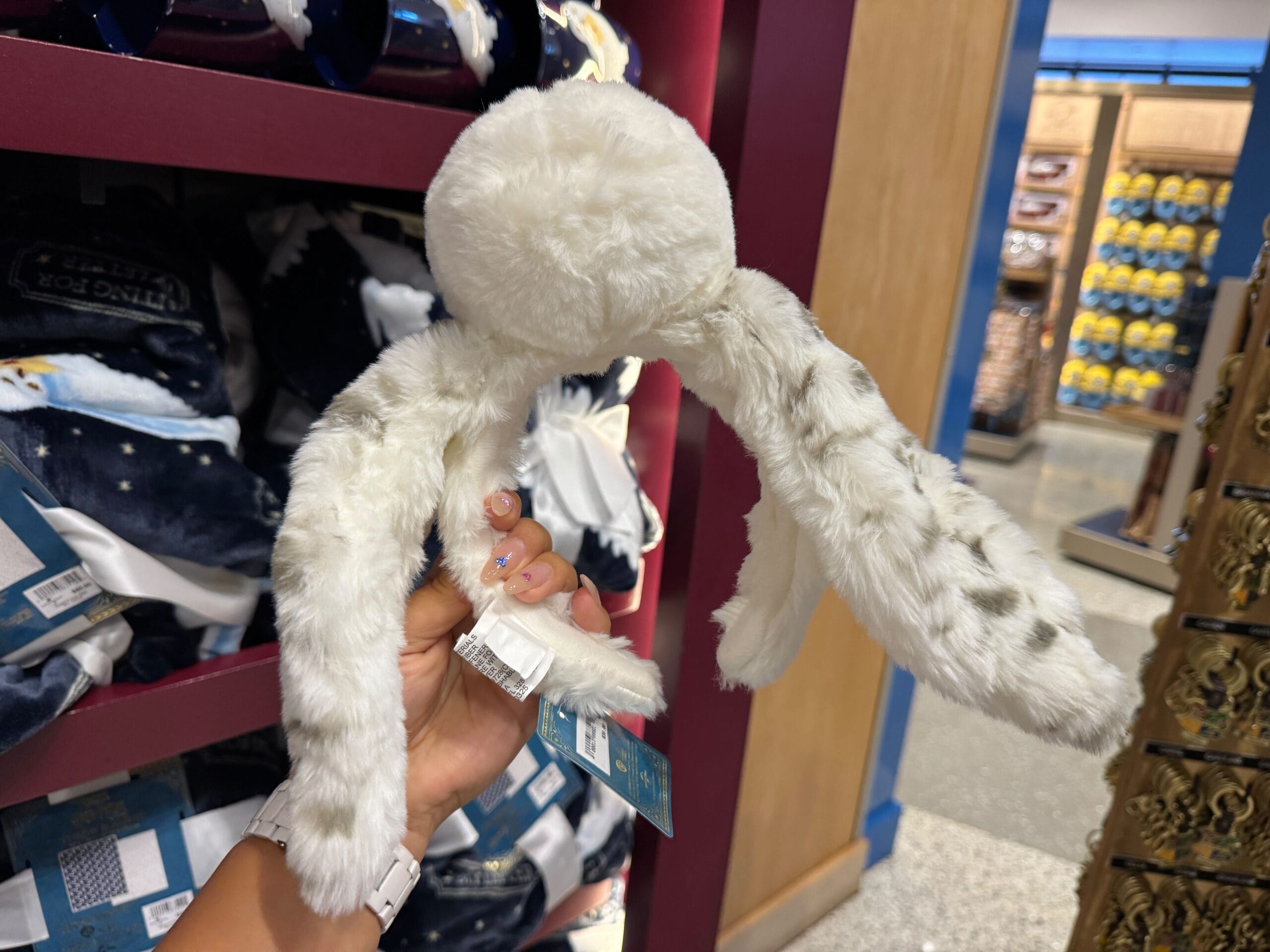 A hand holds a white plush toy with long floppy ears, like Hedwig waiting for a letter, in a store display.