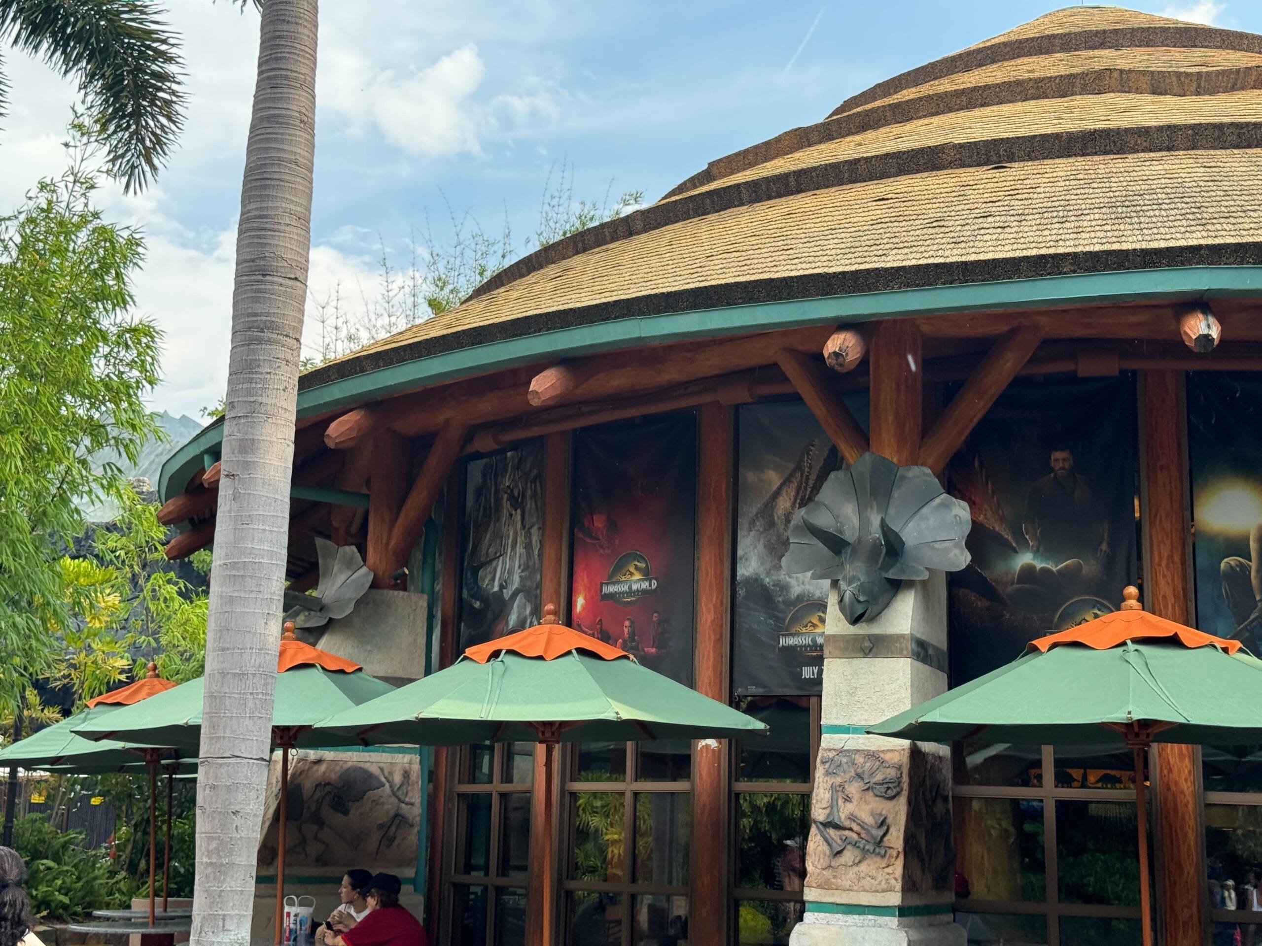 A round building with posters, green umbrellas, and orange trim outside, surrounded by trees and greenery.