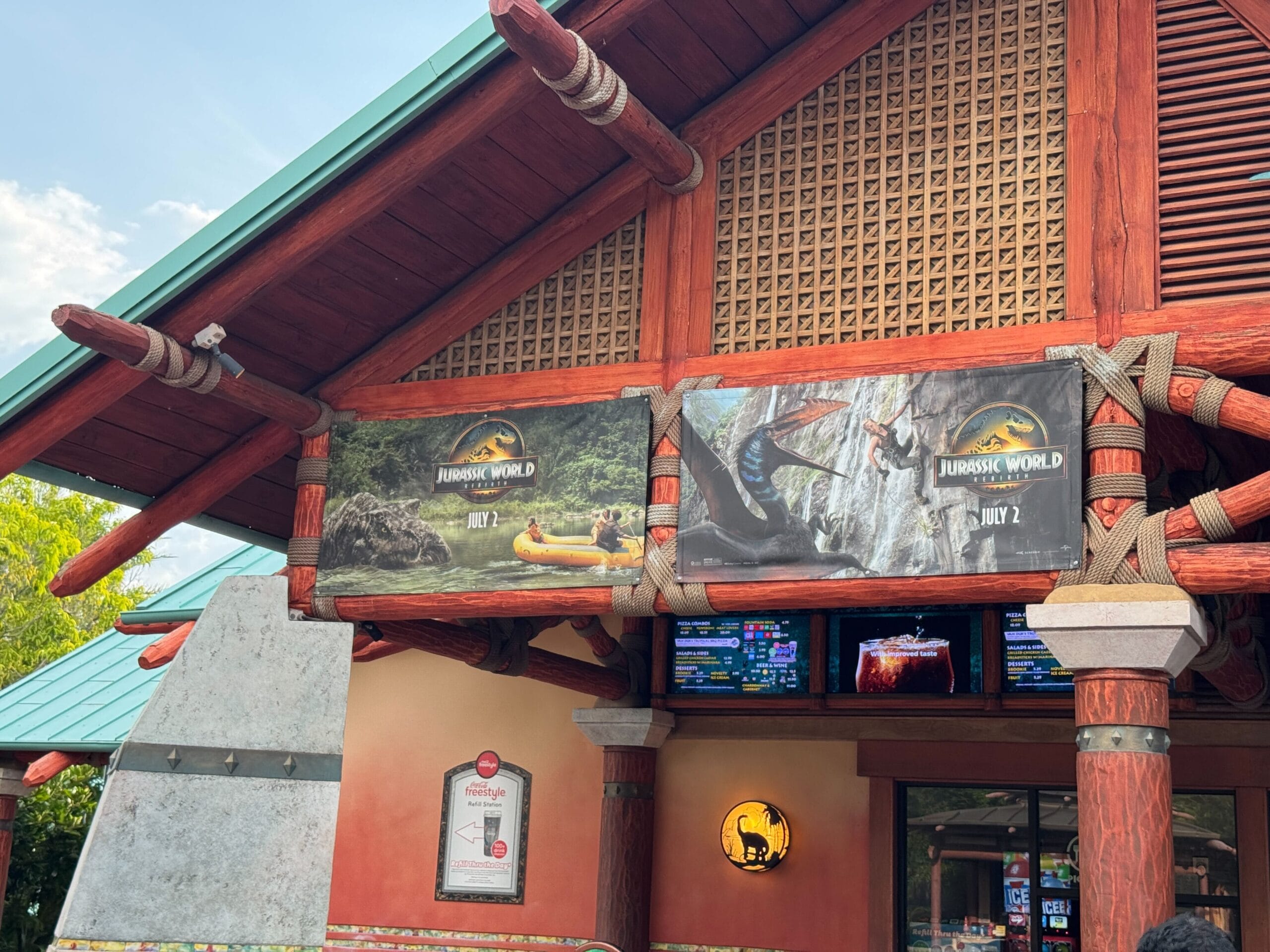 A Jurassic World ride banner is displayed above an entrance with electronic menus and a dinosaur logo.