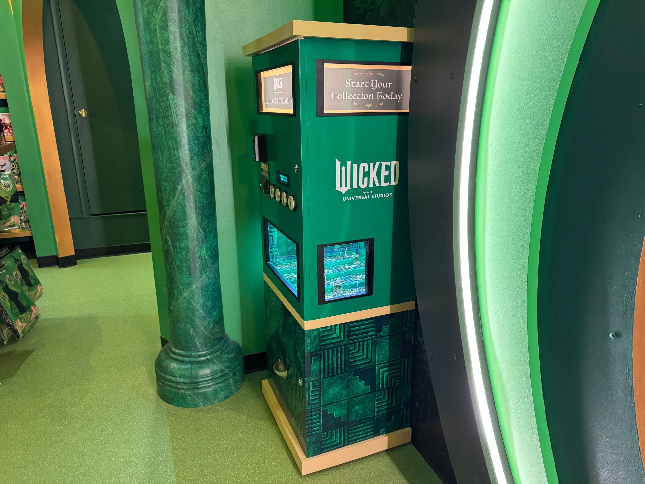 A green "Wicked" Collectible Medallions machine stands in a themed retail area at Universal Studios Florida.