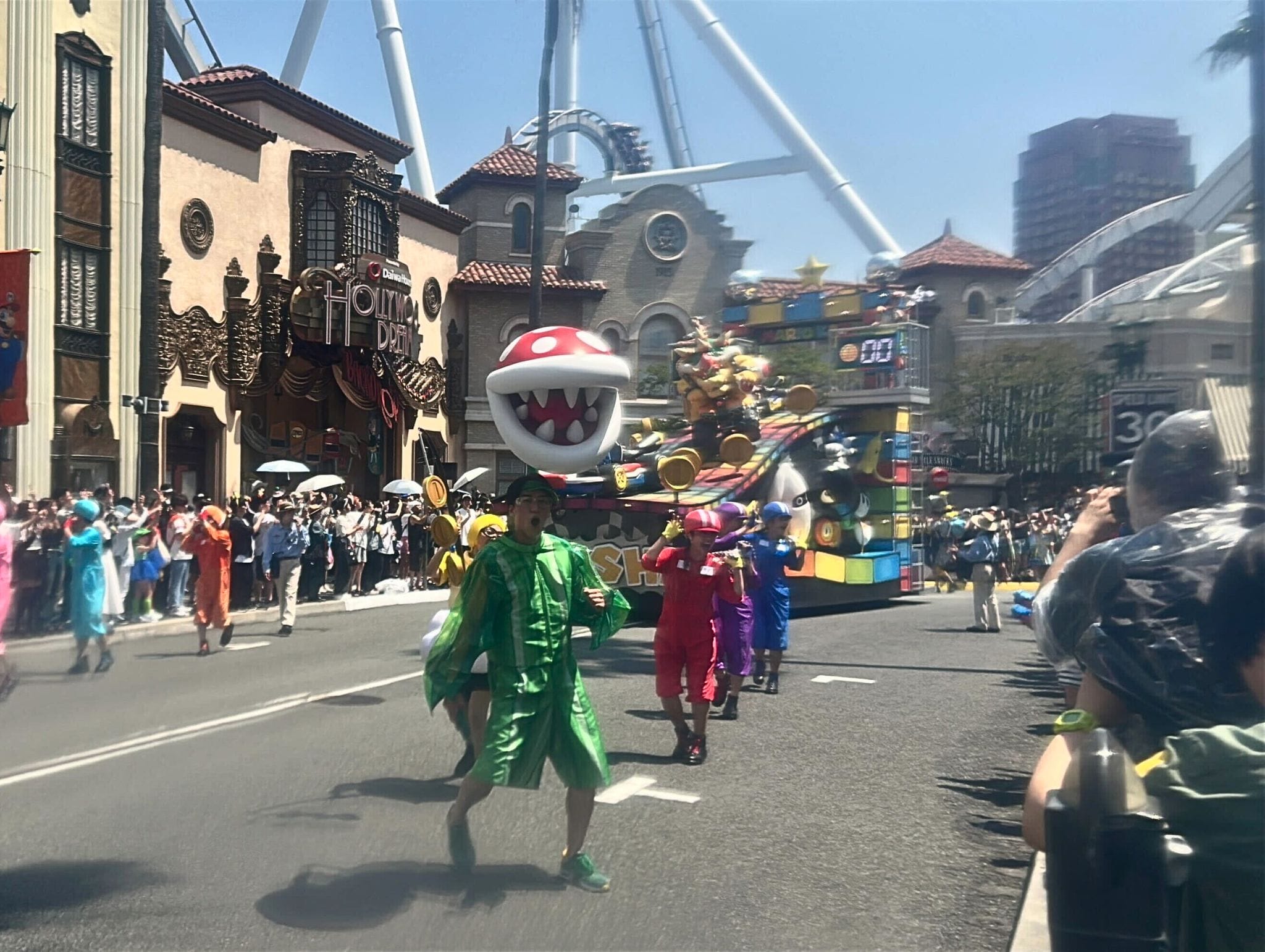 A colorful Summer Splash Parade at Universal Studios Japan features Mario costumes and a giant Piranha Plant on city streets.