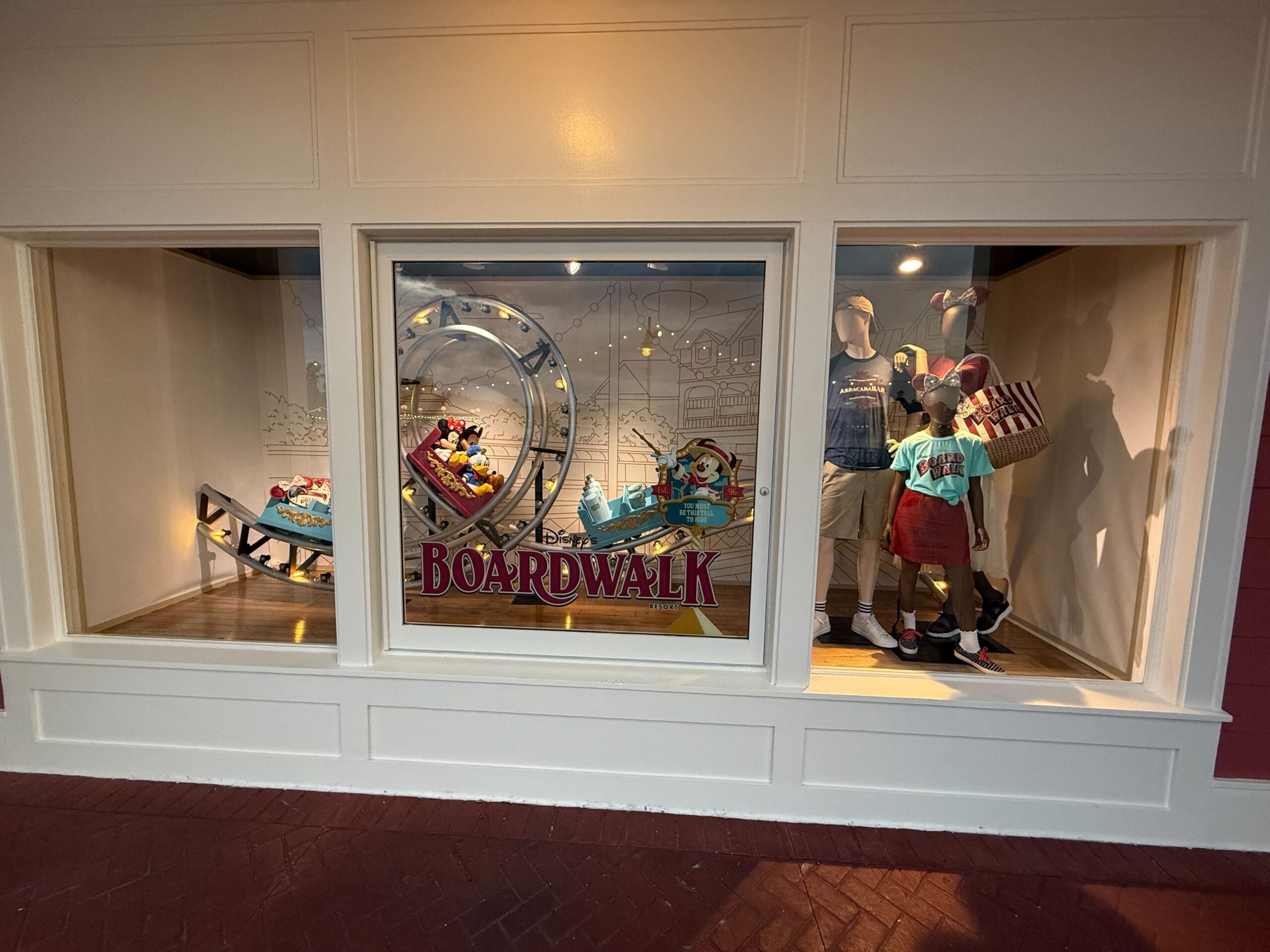 Storefront window display with mannequins, "Boardwalk" sign, and Disney's BoardWalk rollercoaster-themed backdrop.