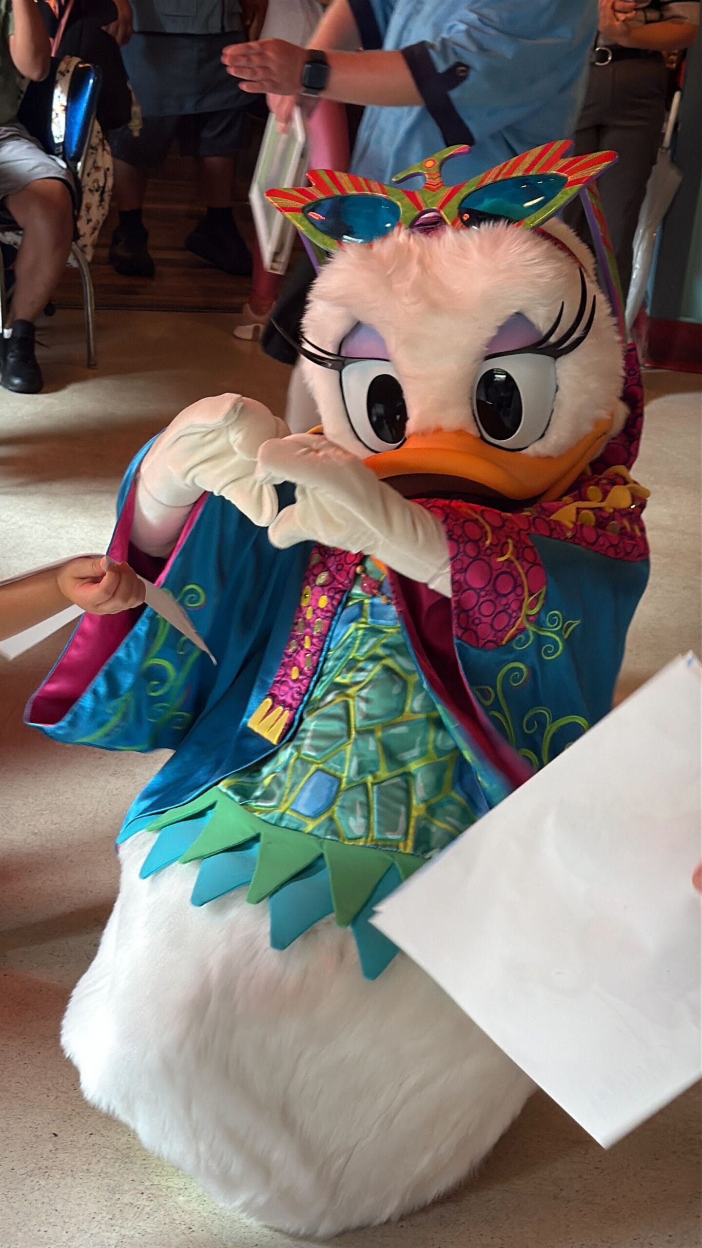 A person in a colorful Daisy Duck costume at Daisy's Dig interacts with children and poses for photos indoors.